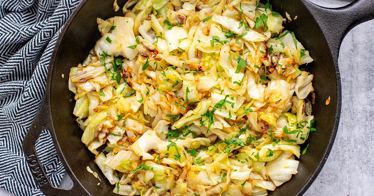 A cast iron skillet filled with sautéed green cabbage with browned edges and visible bits of garlic, resting on a warm-toned kitchen counter