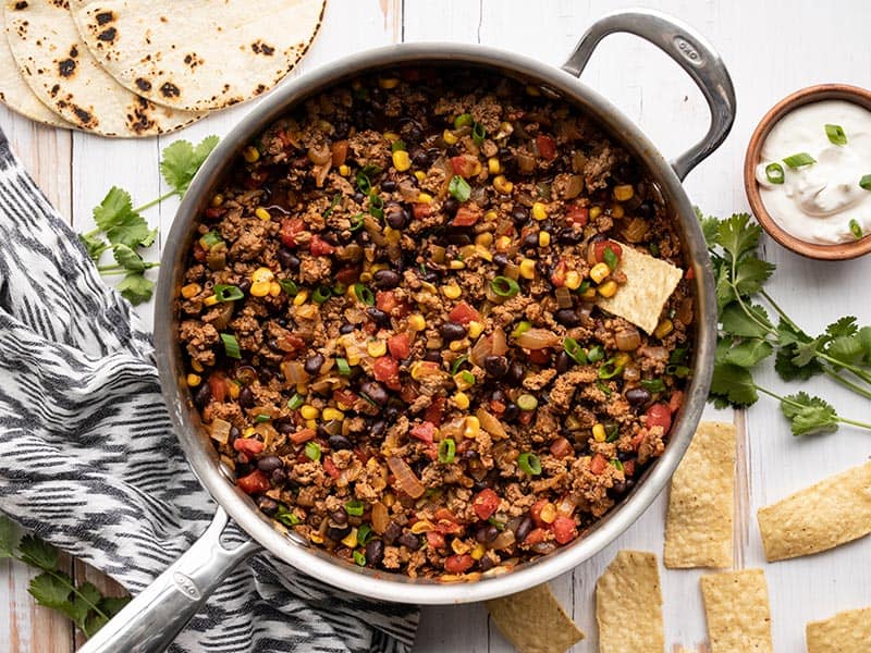 A cast iron skillet filled with seasoned ground turkey, bell peppers, and cauliflower rice, finished with a drizzle of lime yogurt sauce on a wooden kitchen counter