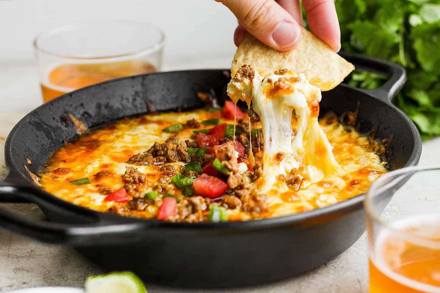 A cast iron skillet of bubbling queso fundido with browned chorizo and roasted poblano strips, garnished with cilantro on a warm kitchen counter
