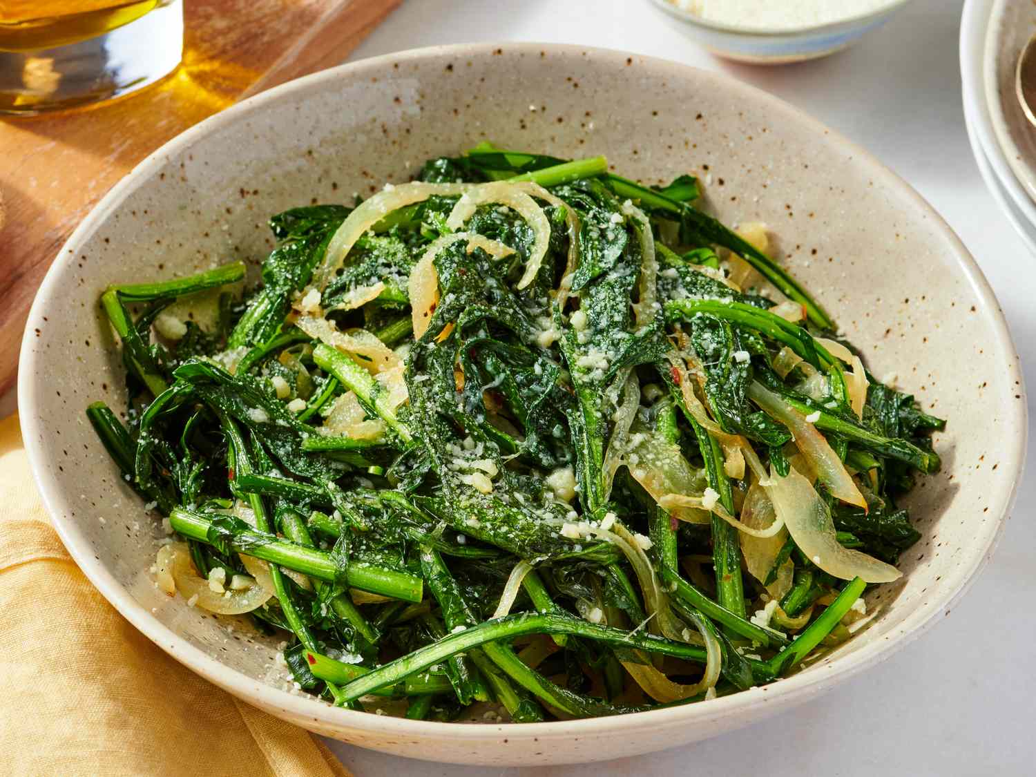 A cast iron skillet of sautéed dandelion greens with golden garlic slices and a lemon wedge on the side, warm kitchen lighting