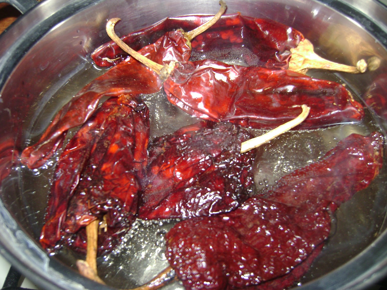 A cast iron skillet on a stovetop with dried chiles and garlic gently toasting, with a wooden spoon stirring them