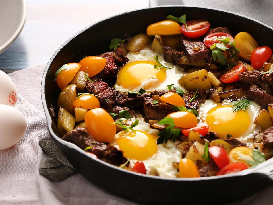 A cast iron skillet with a sliced, medium-rare steak and two sunny-side-up eggs with crisp edges, finished with flaky salt on a warm kitchen counter