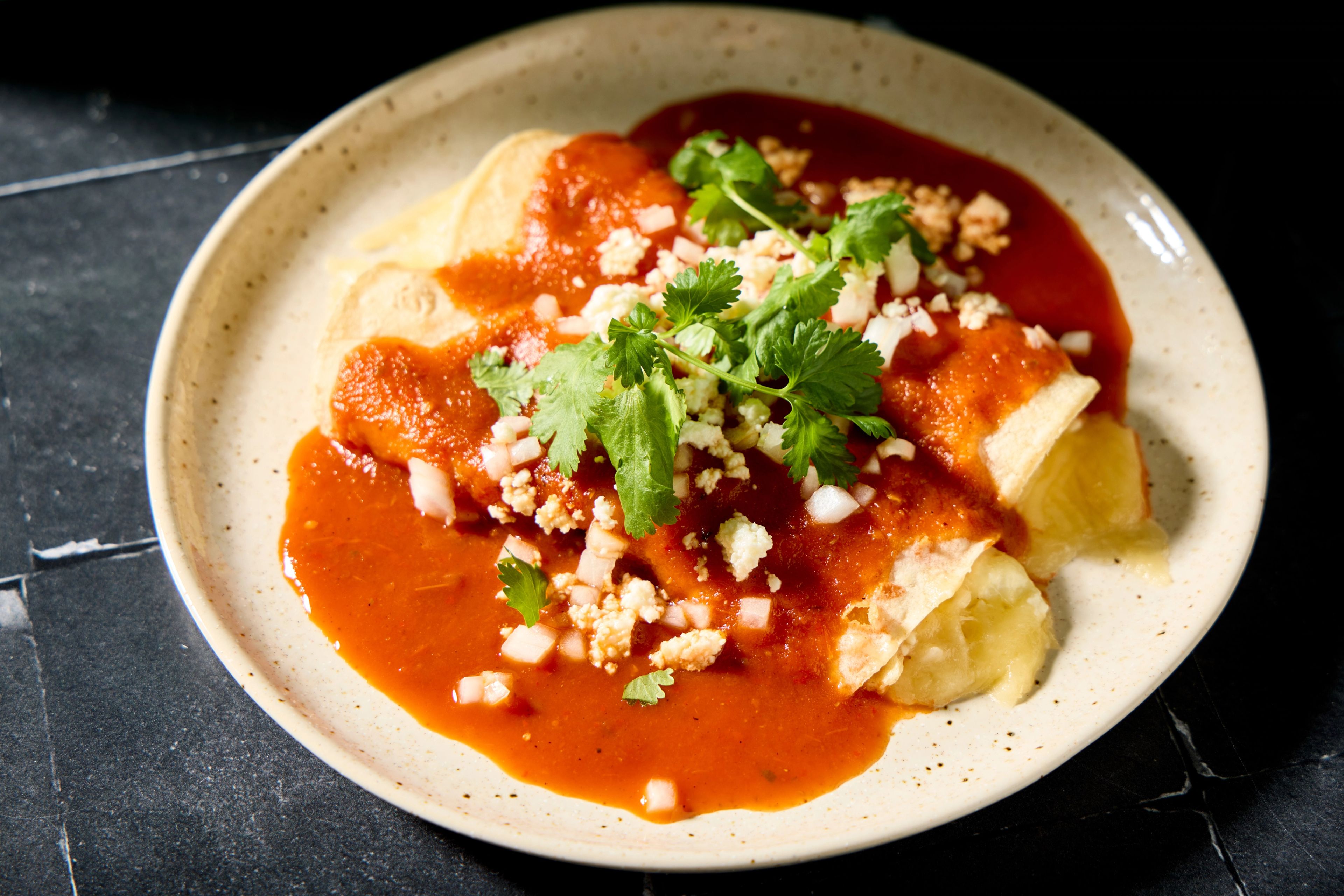 A ceramic baking dish filled with red-sauce cheese enchiladas topped with melted cheese and chopped cilantro on a warm-toned kitchen counter