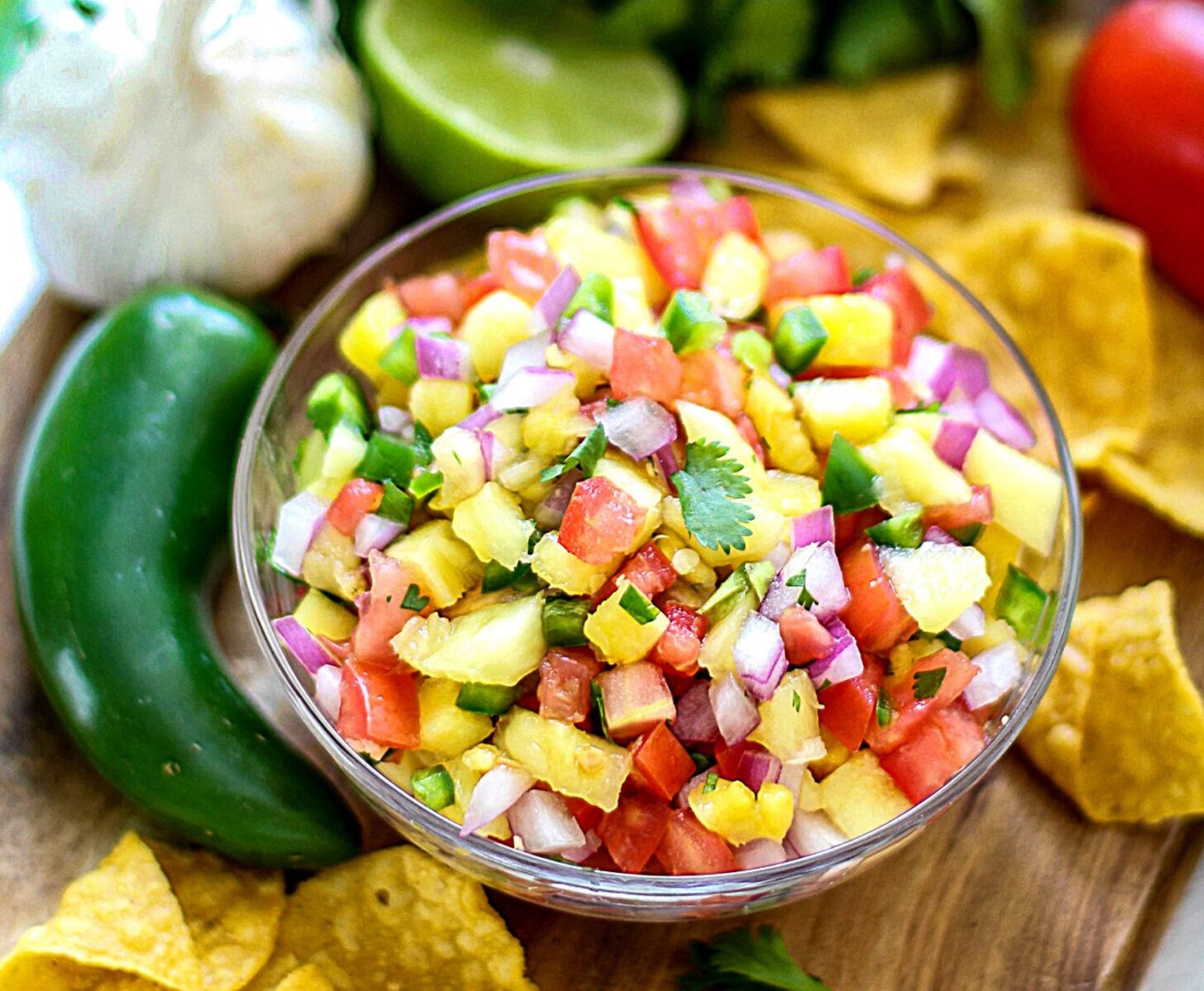 A ceramic bowl filled with diced pineapple salsa with cilantro, onion, and jalapeño on a kitchen counter next to a cut lime