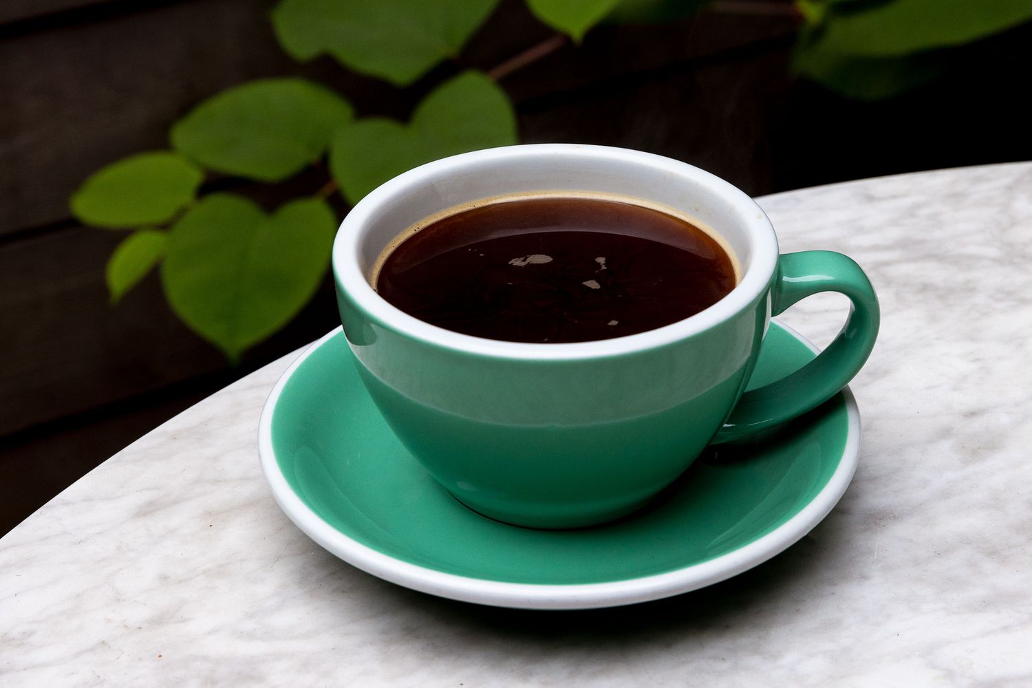 A ceramic mug of hot Americano coffee on a light stone countertop with a spoon nearby and soft morning window light