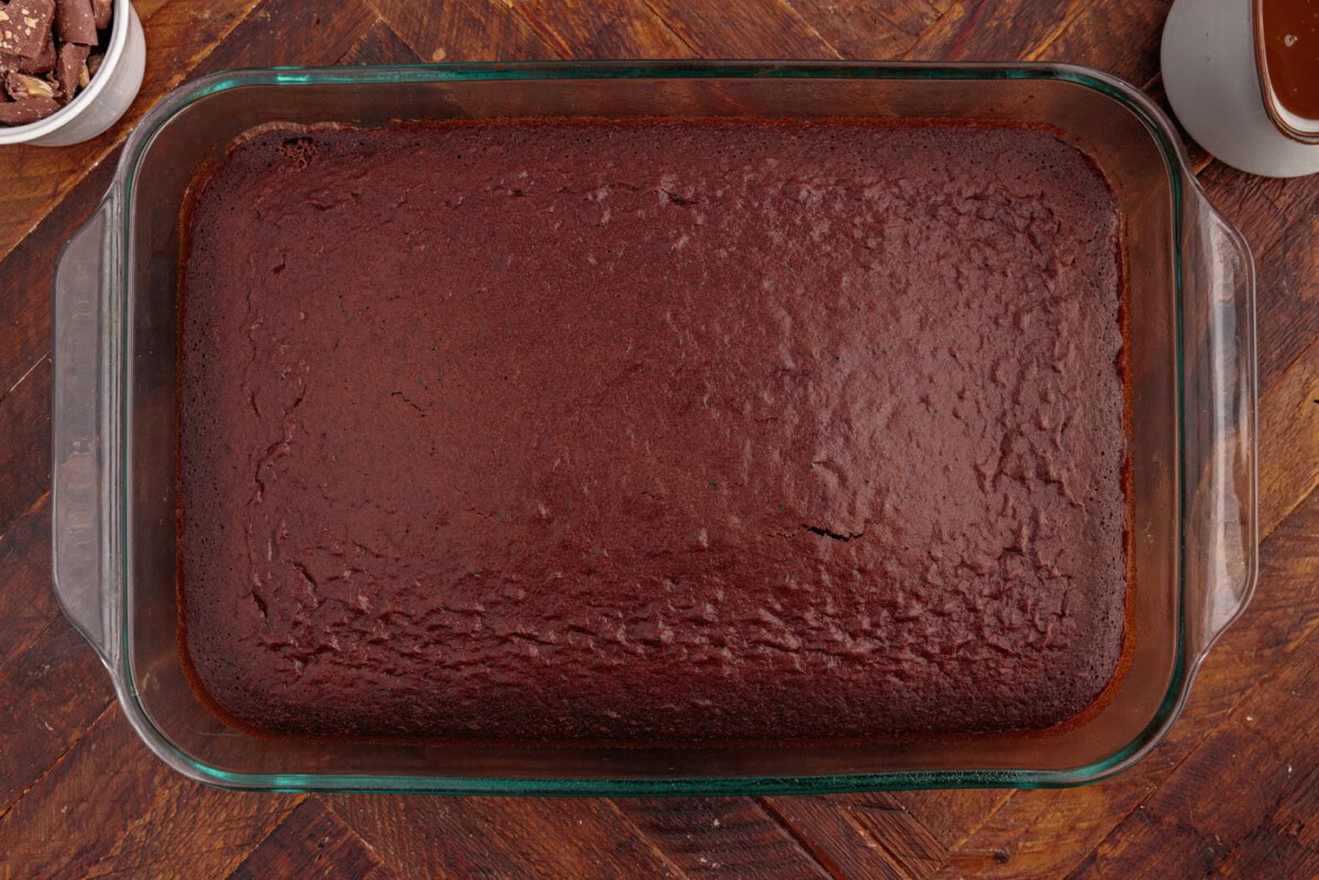 A chilled Better Than Sex Cake in a 9x13 pan with chocolate cake, whipped topping, caramel drizzle, and toffee bits on a bright kitchen counter