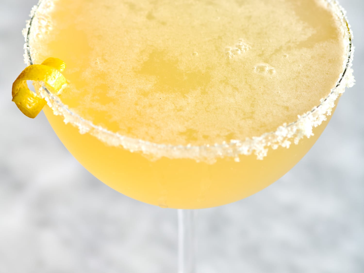 A chilled lemon drop shot in a small glass with a sugared rim and a thin lemon twist on a bright kitchen counter in natural light