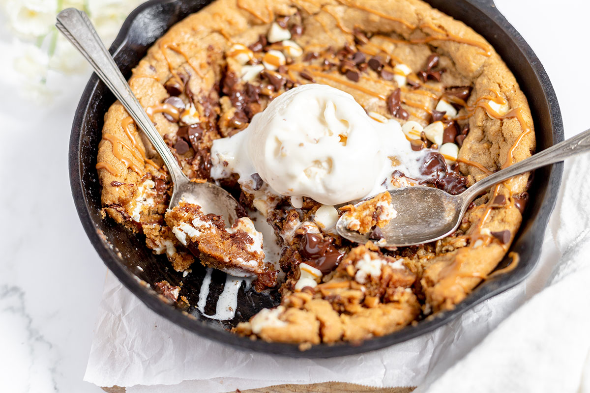A chilled loaf pan of pale ice cream base with Biscoff cookie butter swirled through the top using a butter knife on a bright kitchen counter