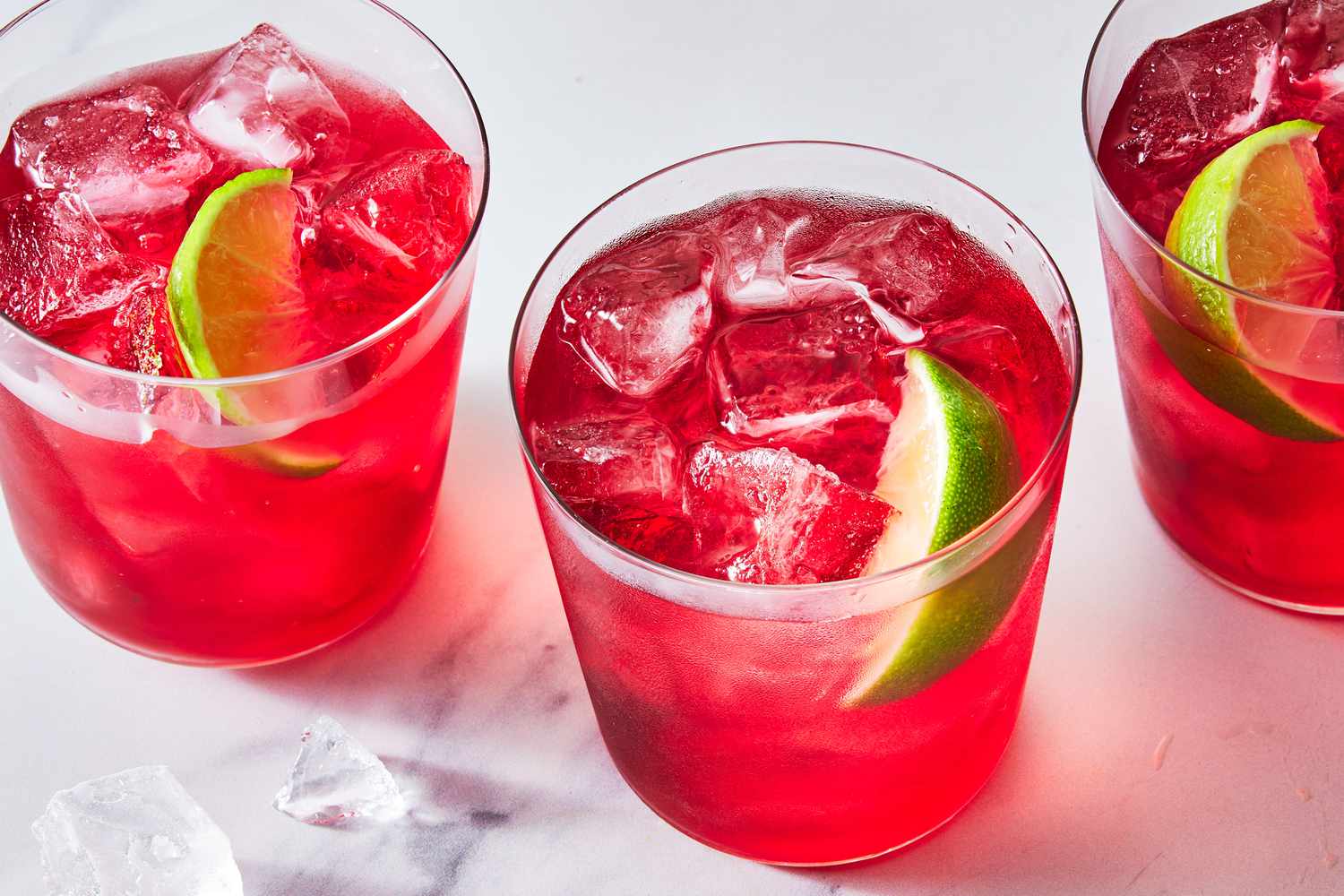 A chilled vodka cranberry cocktail in a clear highball glass filled with ice, garnished with a lime wedge and a few fresh cranberries on a neutral kitchen counter with soft natural light