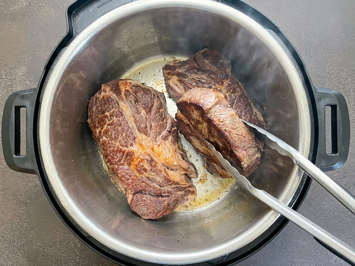 A chuck roast browning in an Instant Pot inner pot on sauté mode, with caramelized edges forming