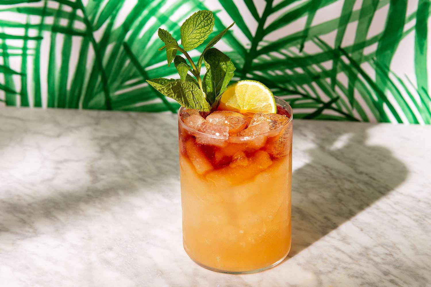 A classic Mai Tai in a double old fashioned glass filled with crushed ice, garnished with a mint sprig and a spent lime shell on a warm kitchen counter with soft natural light