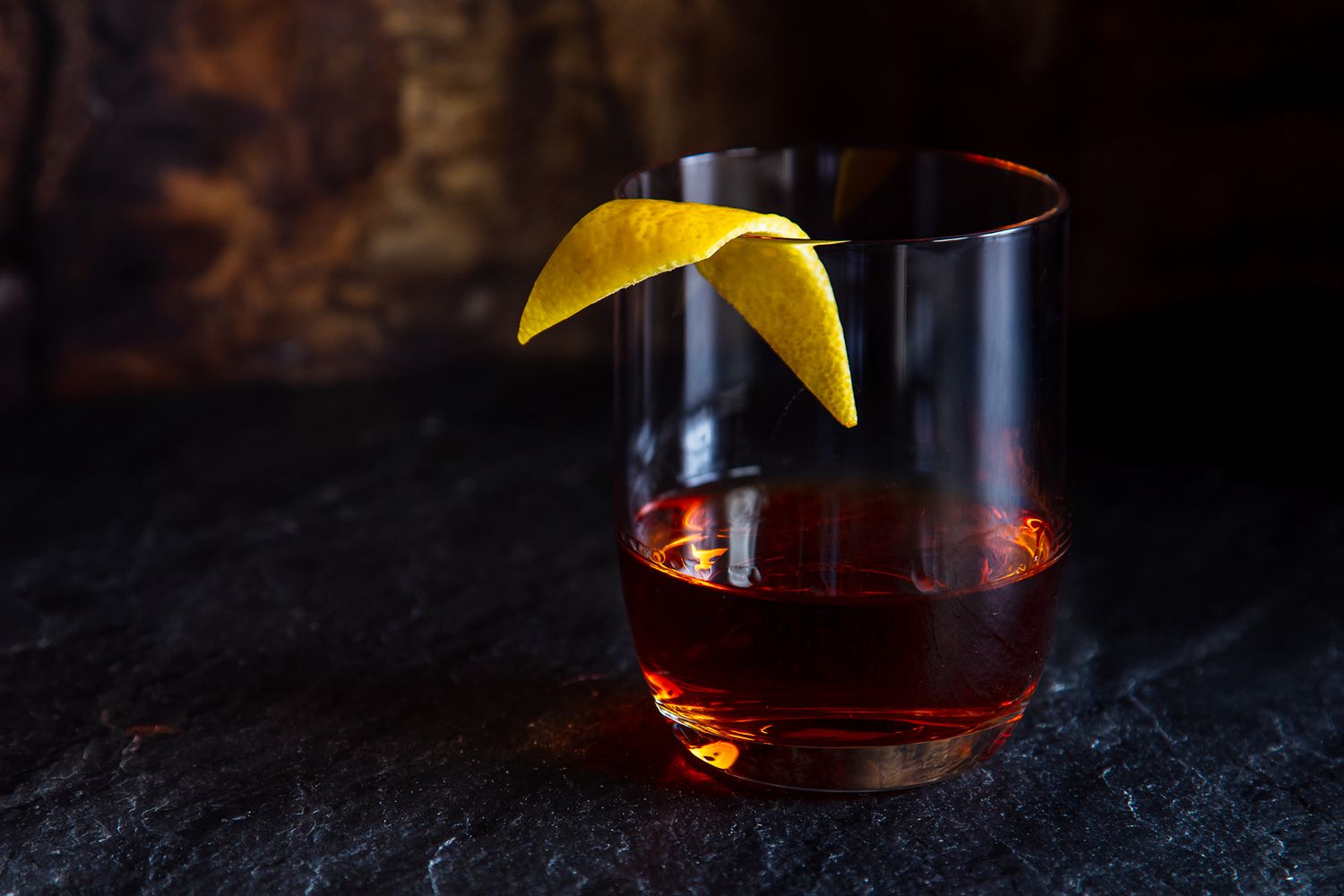A classic Sazerac cocktail served in a chilled rocks glass with a lemon peel expressed over the top, on a warm-toned kitchen counter with soft evening light