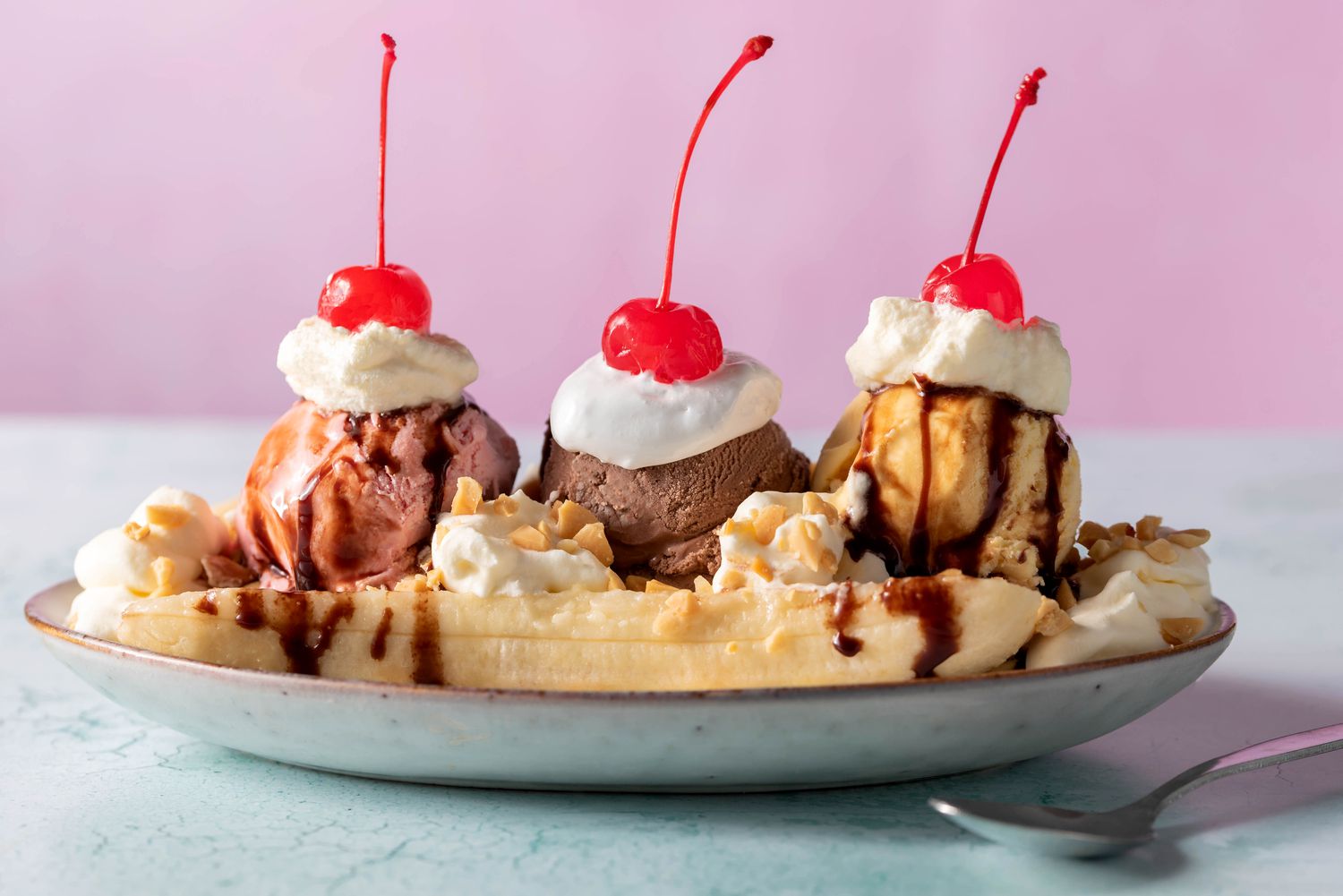A classic banana split in a long glass dish with a split banana, three scoops of vanilla, chocolate, and strawberry ice cream, chocolate syrup, strawberry topping, pineapple topping, whipped cream, chopped nuts, and maraschino cherries on a bright kitchen counter