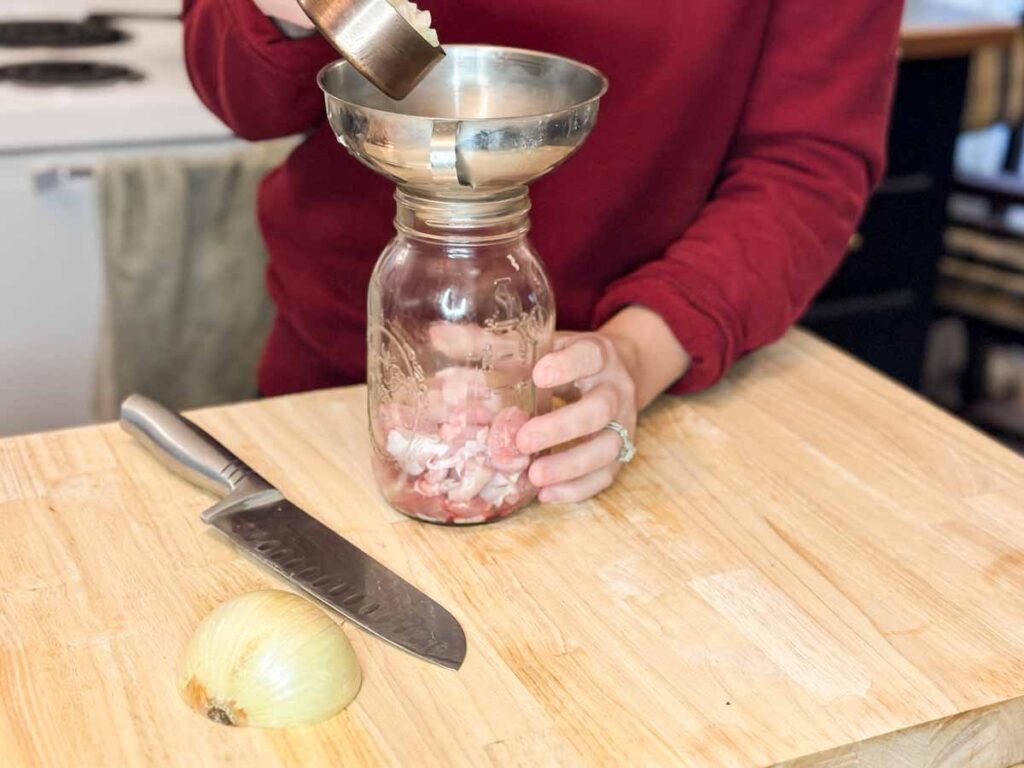 A clean quart mason jar with lid, a small saucepan, and a cutting board set up for making refrigerator pickles
