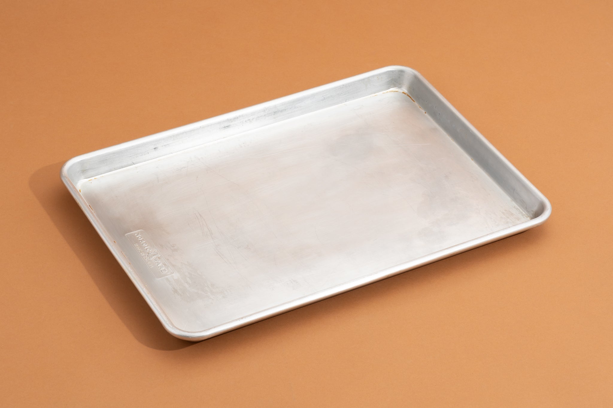A clean rimmed baking sheet lined with parchment paper on a bright kitchen counter beside a rolling pin