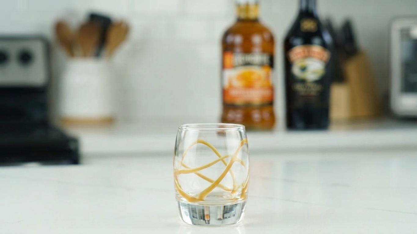 A clean shot glass with a thin swirl of caramel sauce clinging to the inside