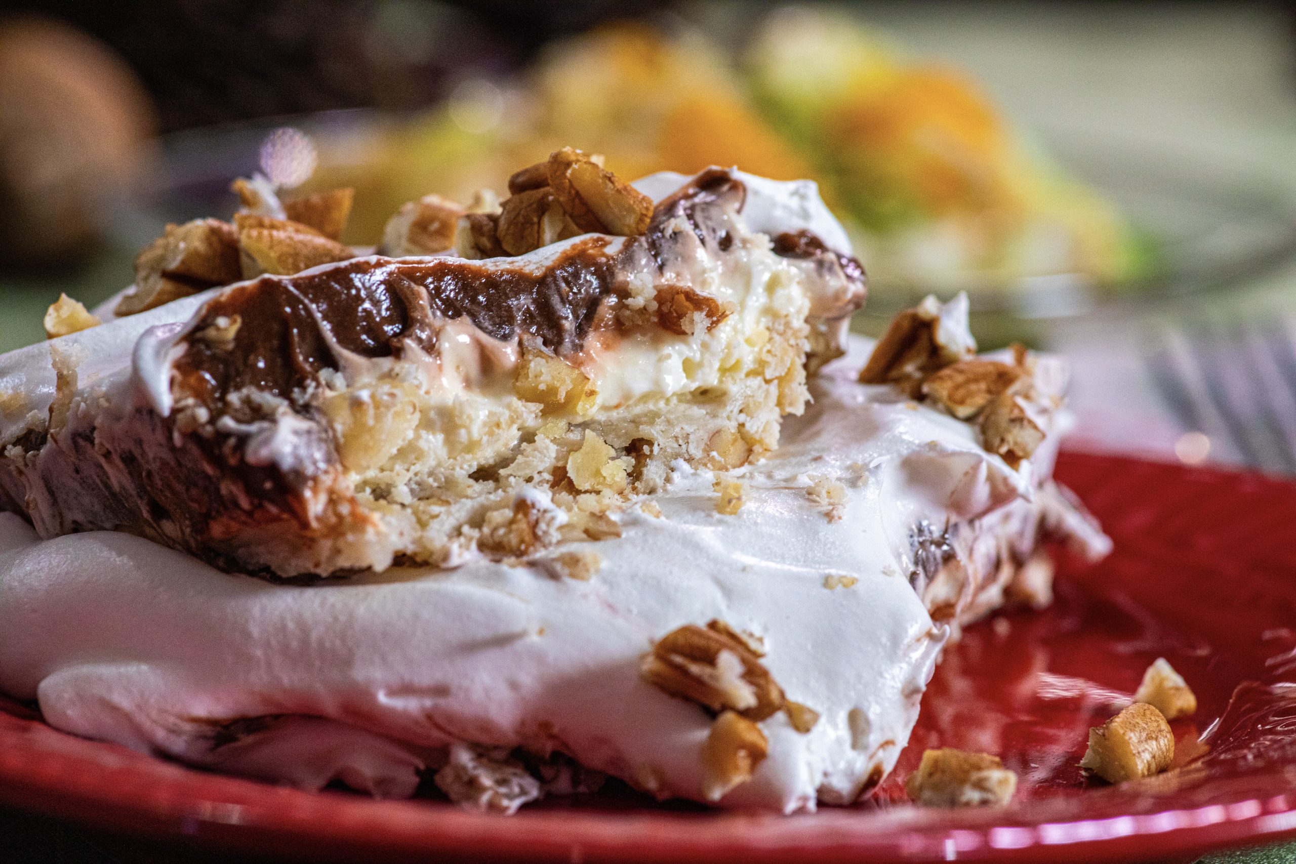 A cleanly sliced piece of chocolate delight dessert on a white plate, showing distinct layers of Oreo crust, creamy cheesecake filling, chocolate pudding, and whipped topping on a bright kitchen counter