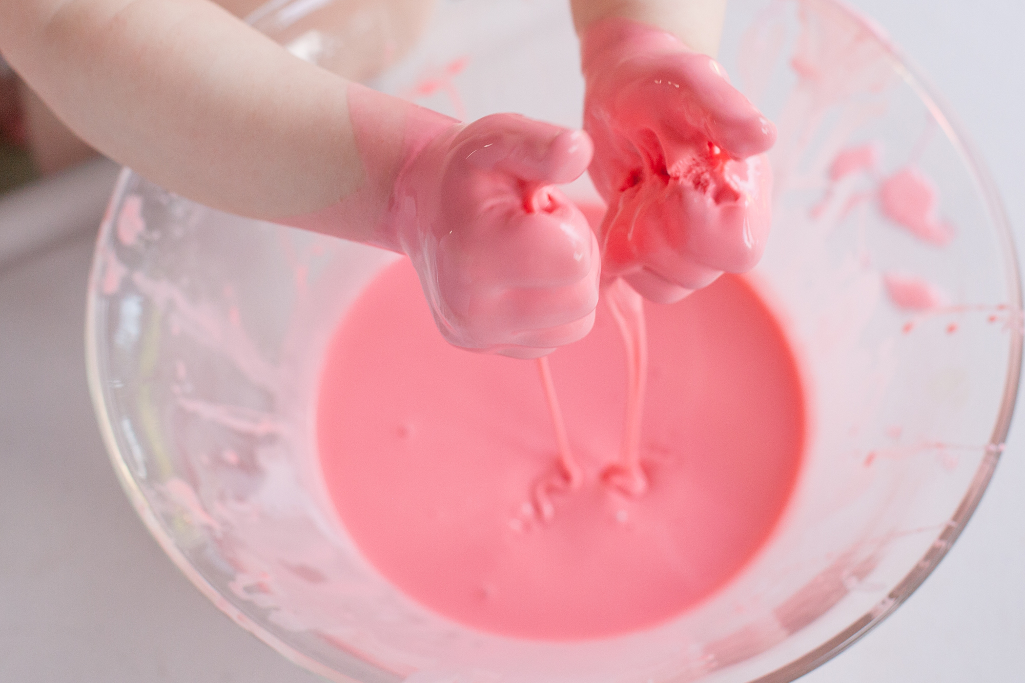 A clear glass bowl of glossy white borax slime on a light kitchen counter with a wooden spoon nearby