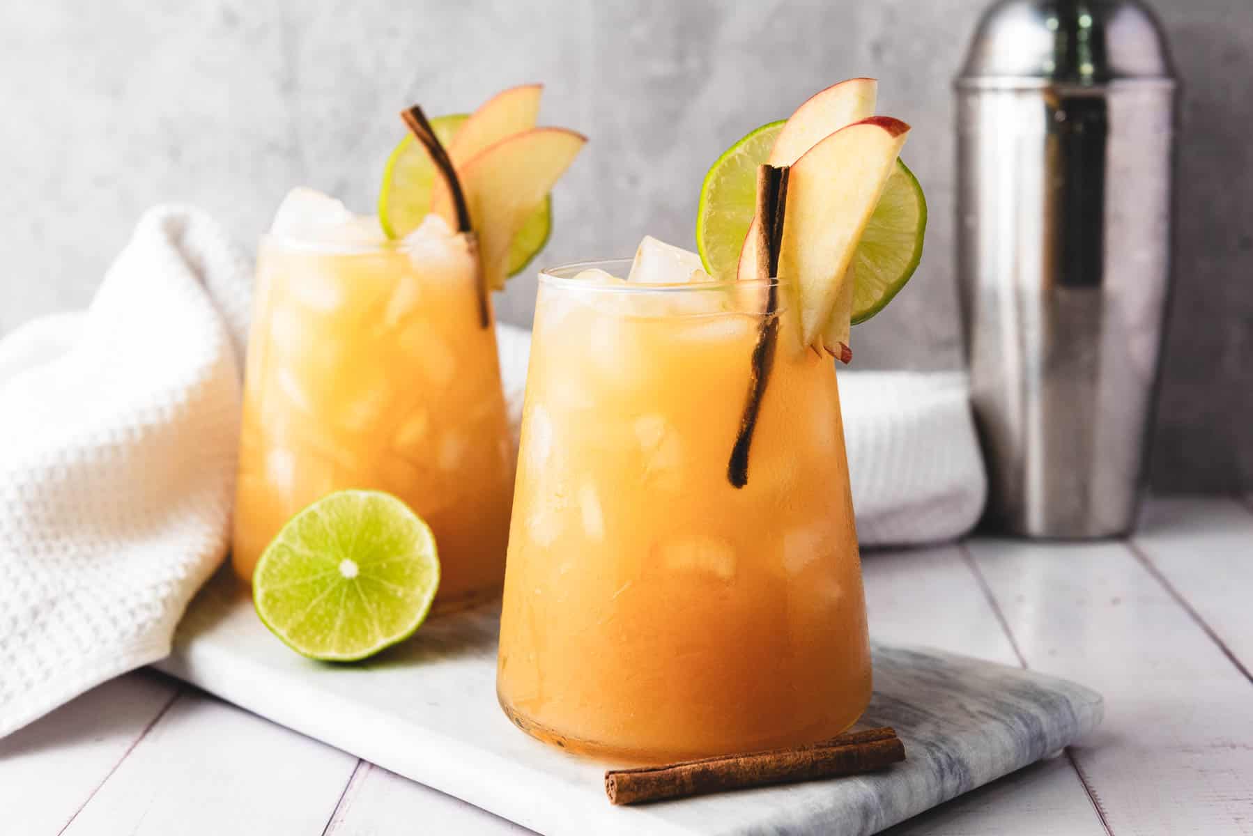 A clear glass filled with an ice cold red mocktail, topped with ginger beer and garnished with an orange wheel and cinnamon stick on a warm kitchen counter