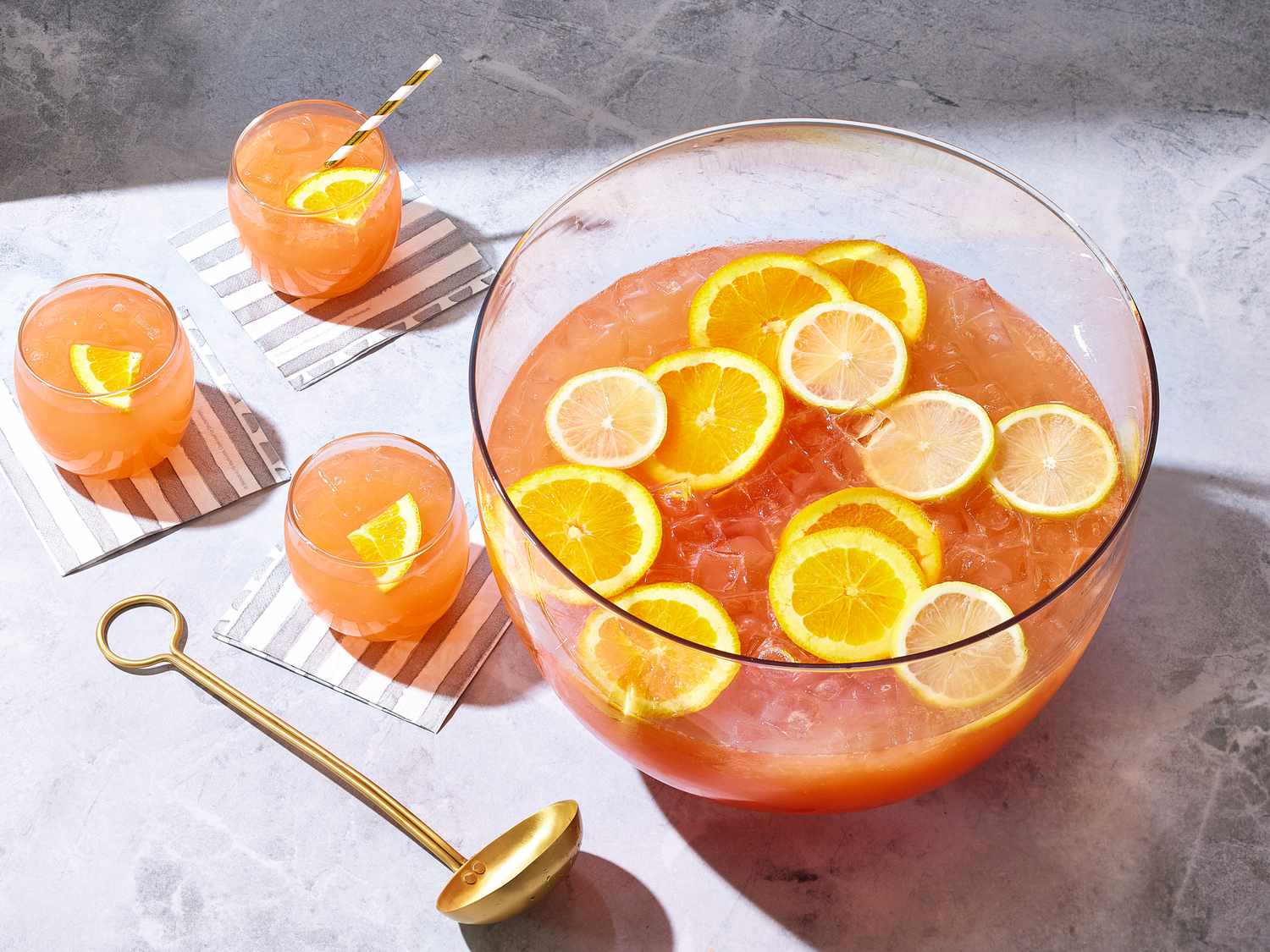A clear glass punch bowl filled with red fruit punch, floating orange and lemon slices, and a ring of ice on a bright kitchen counter with soft natural light
