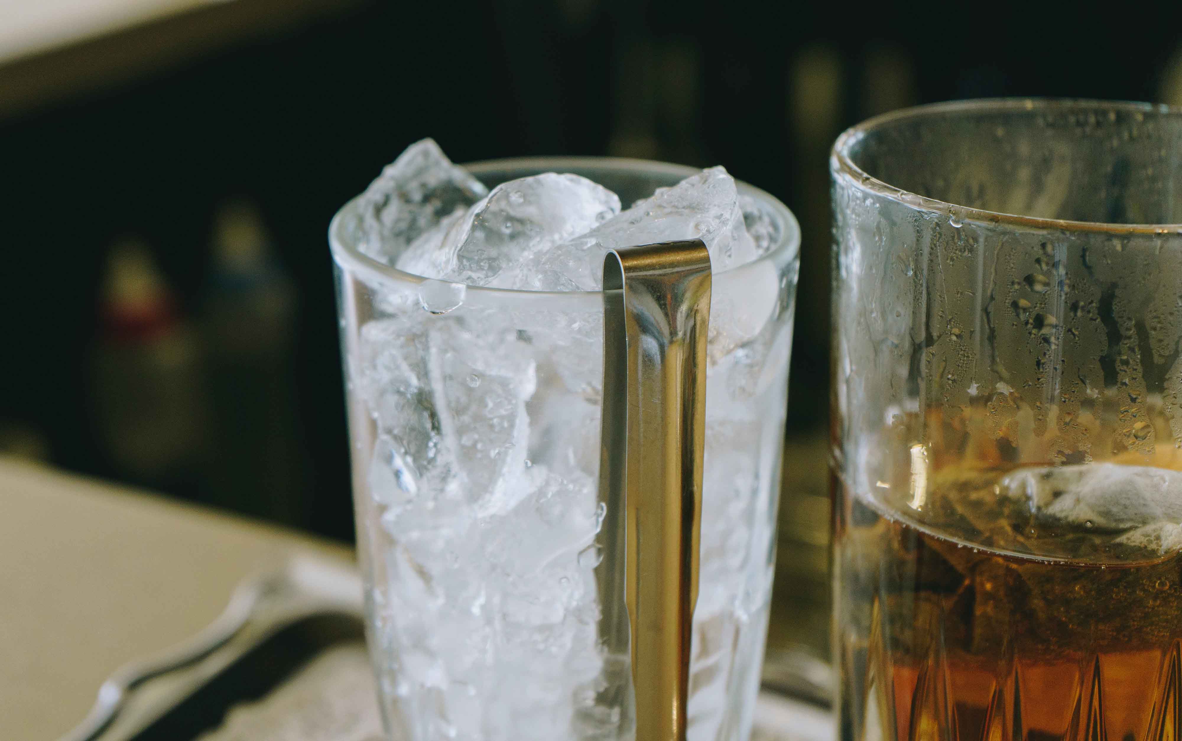 A clear highball glass being filled with large ice cubes on a kitchen counter