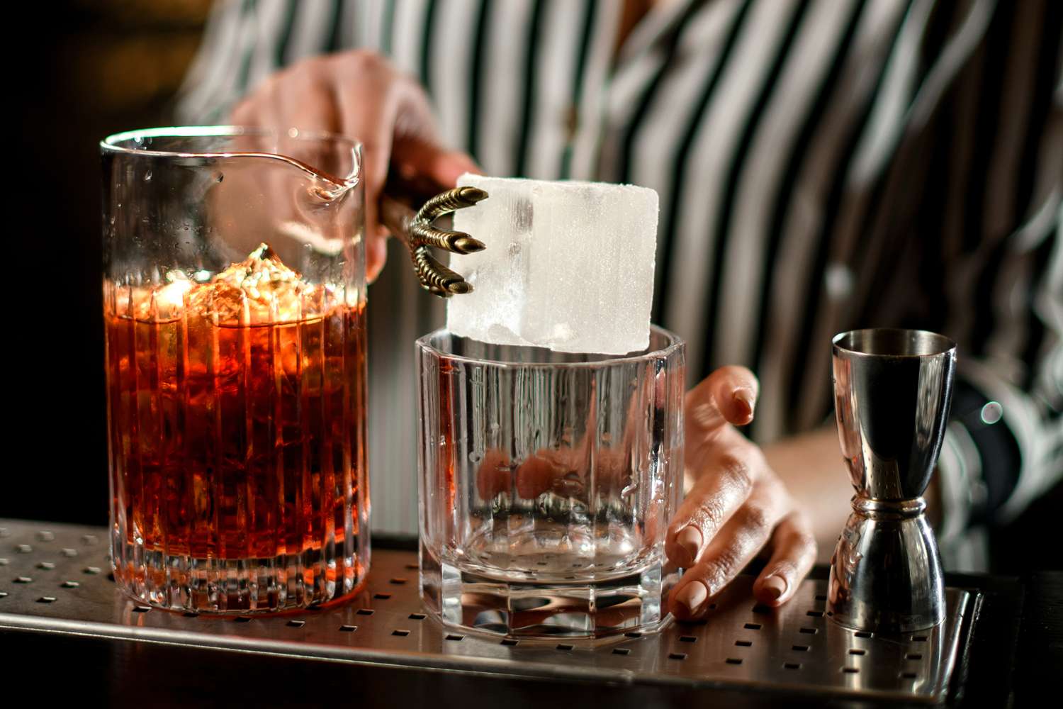 A clear rocks glass on a kitchen counter holding a large clear ice cube, ready for a cocktail