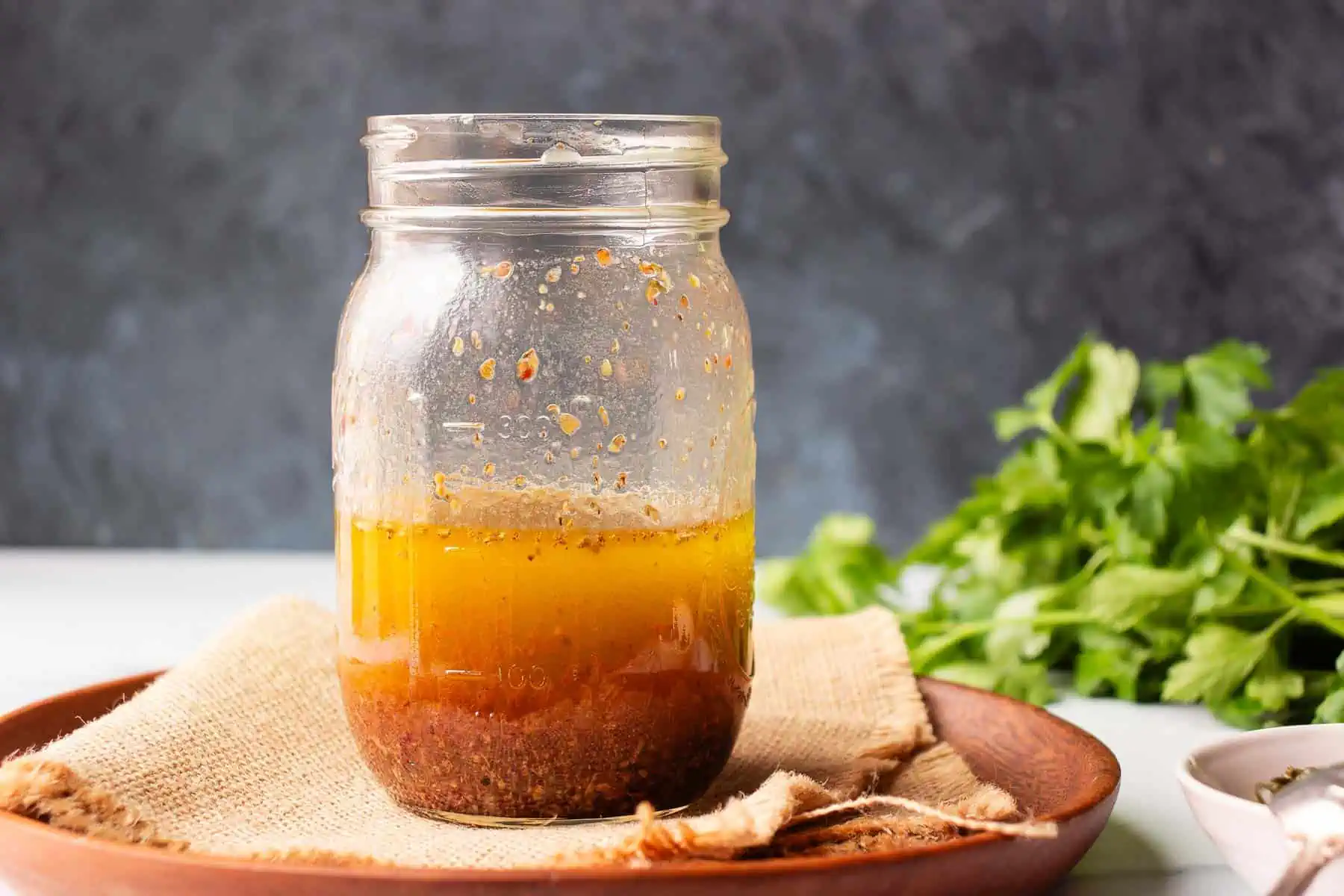 A close-up of Italian salad dressing in a glass jar with herbs and minced garlic suspended after shaking