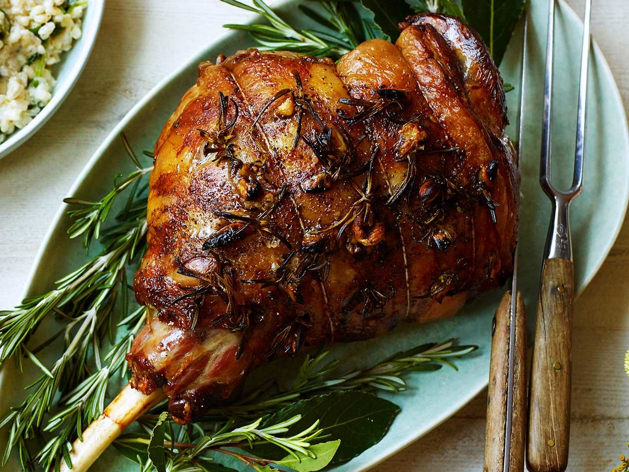 A close-up of a boneless leg of lamb coated in a rosemary garlic mustard rub in a roasting pan
