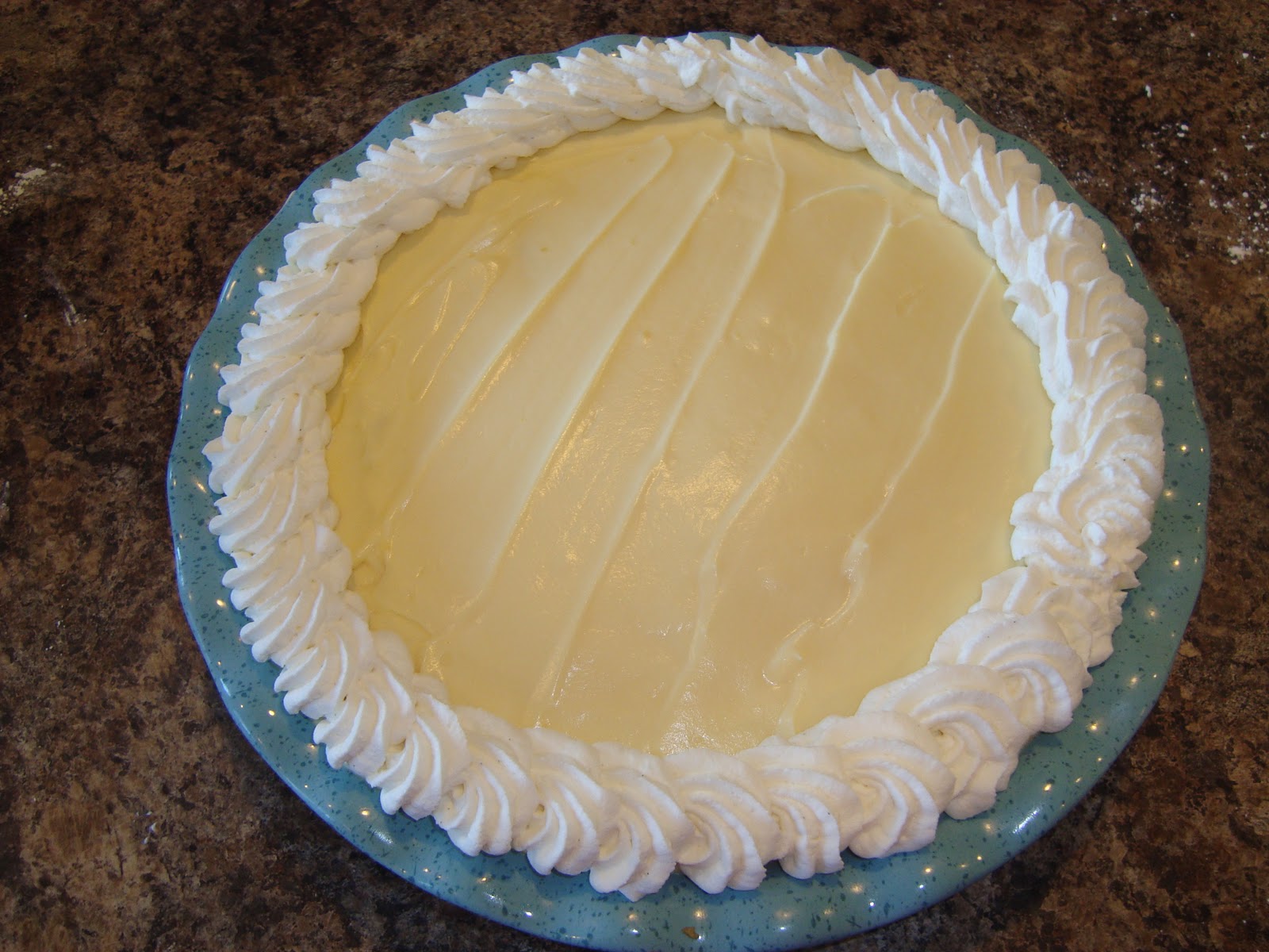 A close-up of a creamy vanilla gel being piped in a neat border along the edge of a whipped-cream topped dessert on a light kitchen counter