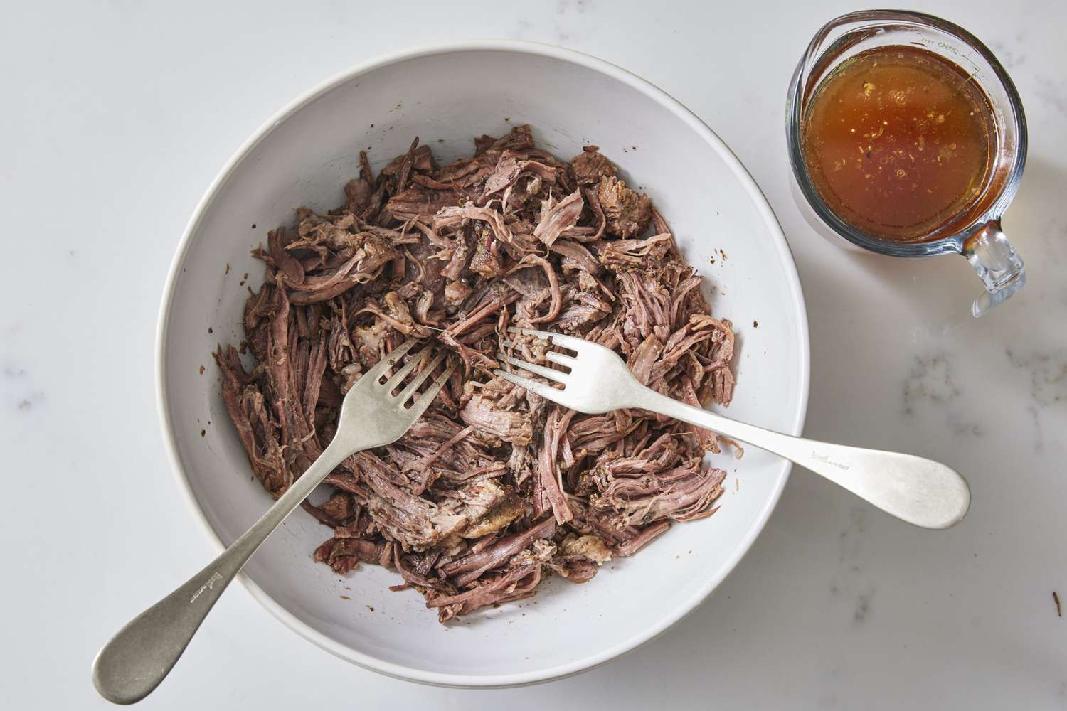 A close-up of a fork pulling apart tender oven-braised chuck roast on a plate with gravy, showing moist shredded strands