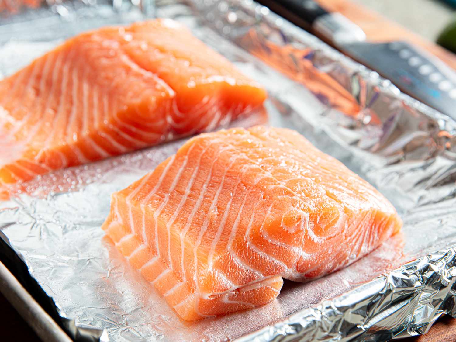 A close-up of a hand using a small knife to cut a pocket into the side of a raw salmon fillet on a cutting board