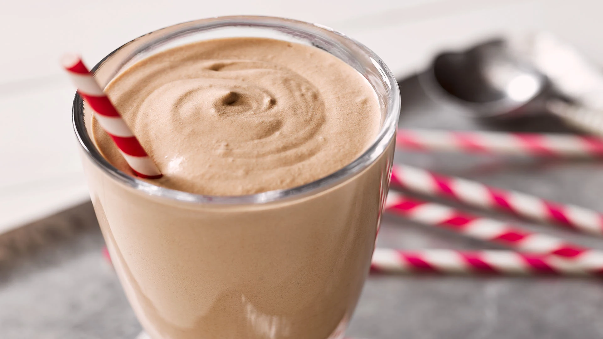 A close-up of cocoa powder, vanilla ice cream scoops, and a small pitcher of milk set on a kitchen counter ready to blend
