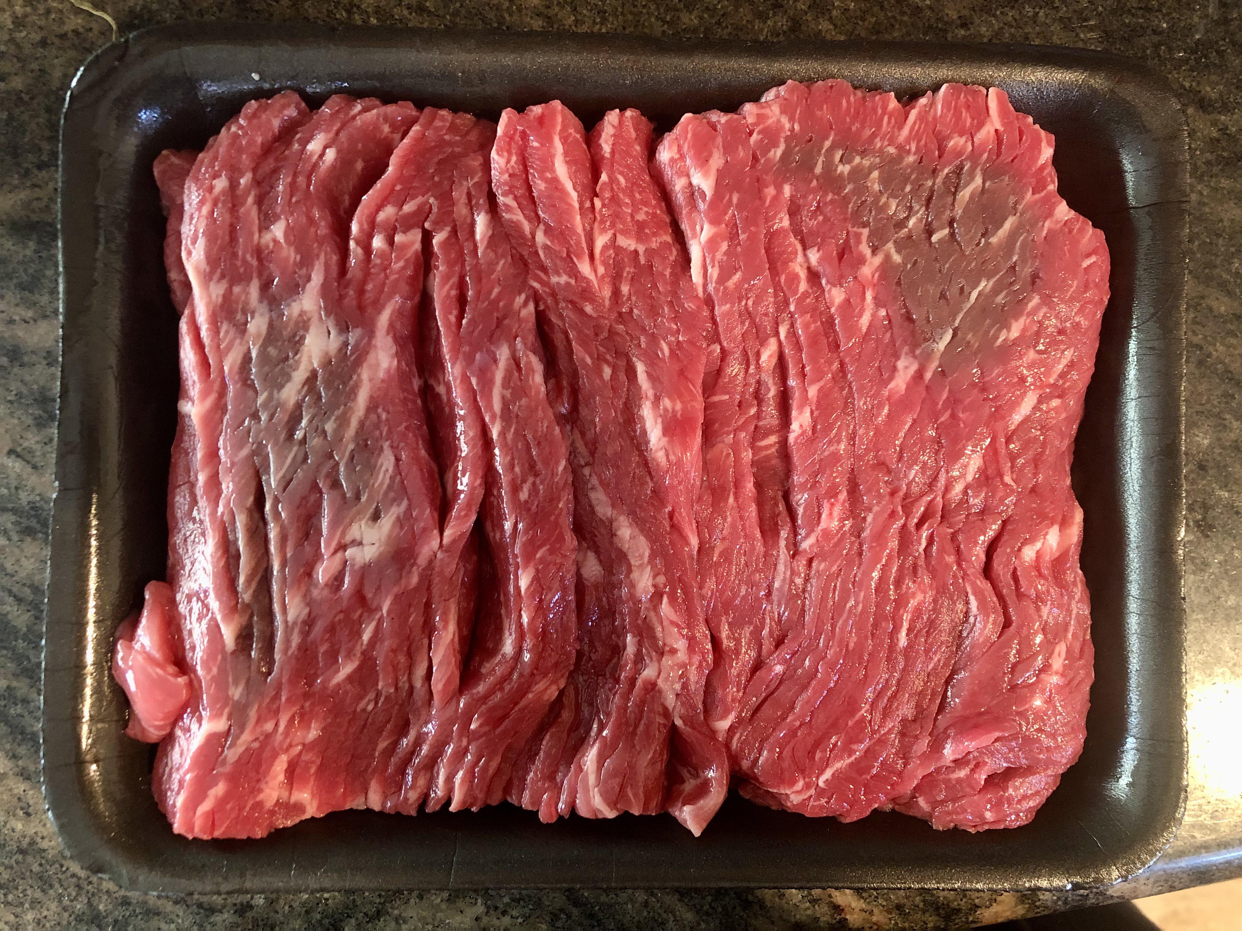 A close-up of neatly rolled thin-sliced beef on a plate, ready for hot pot cooking