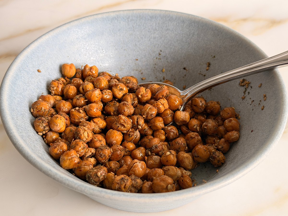 A close-up of roasted chickpeas in a small bowl with visible crunchy texture and a pinch of flaky salt