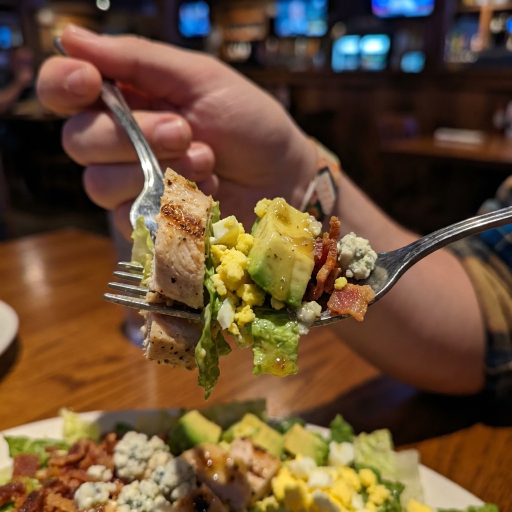 A close-up photo of a fork lifting a bite of Cobb salad with chicken, avocado, egg, and vinaigrette