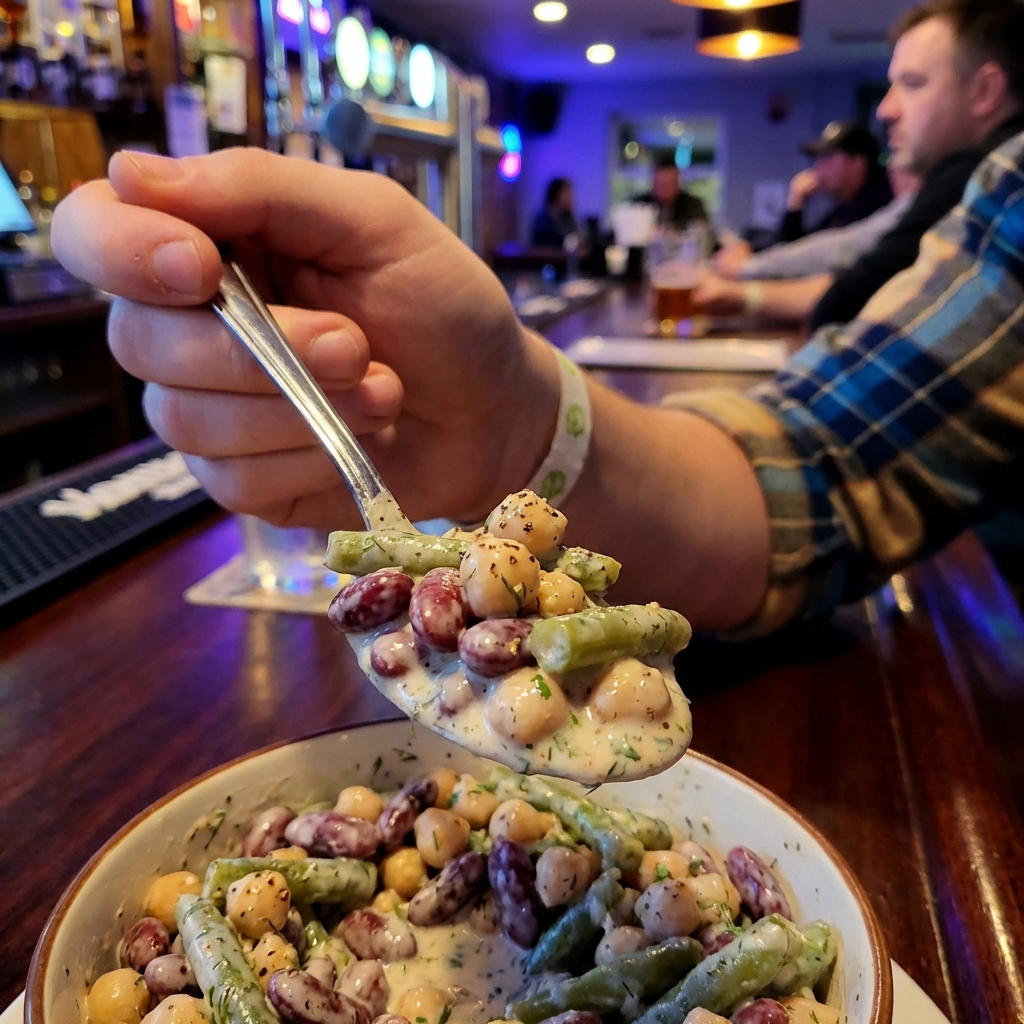 A close-up photo of a spoon lifting creamy bean salad showing beans coated in a light dressing with chopped herbs