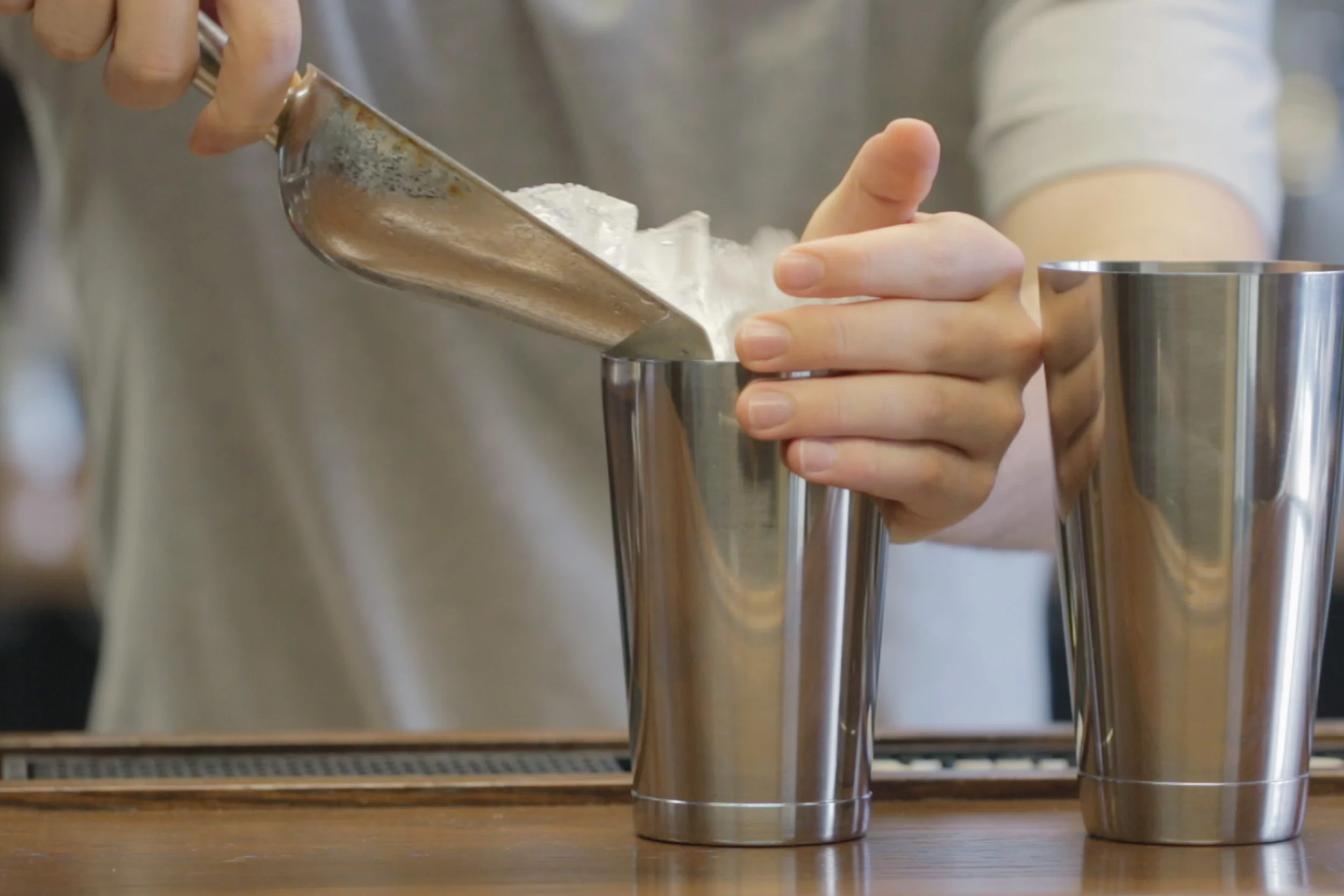 A cocktail shaker filled with ice while measured spirits are added on a kitchen counter