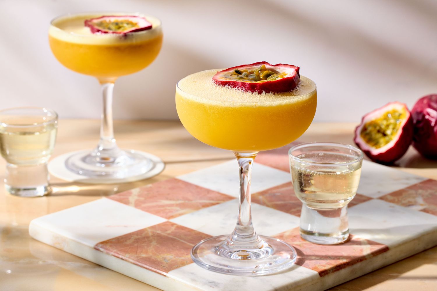 A cocktail shaker on a kitchen counter beside a cut lime, measuring jigger, passion fruit purée, and vanilla vodka ready to be mixed