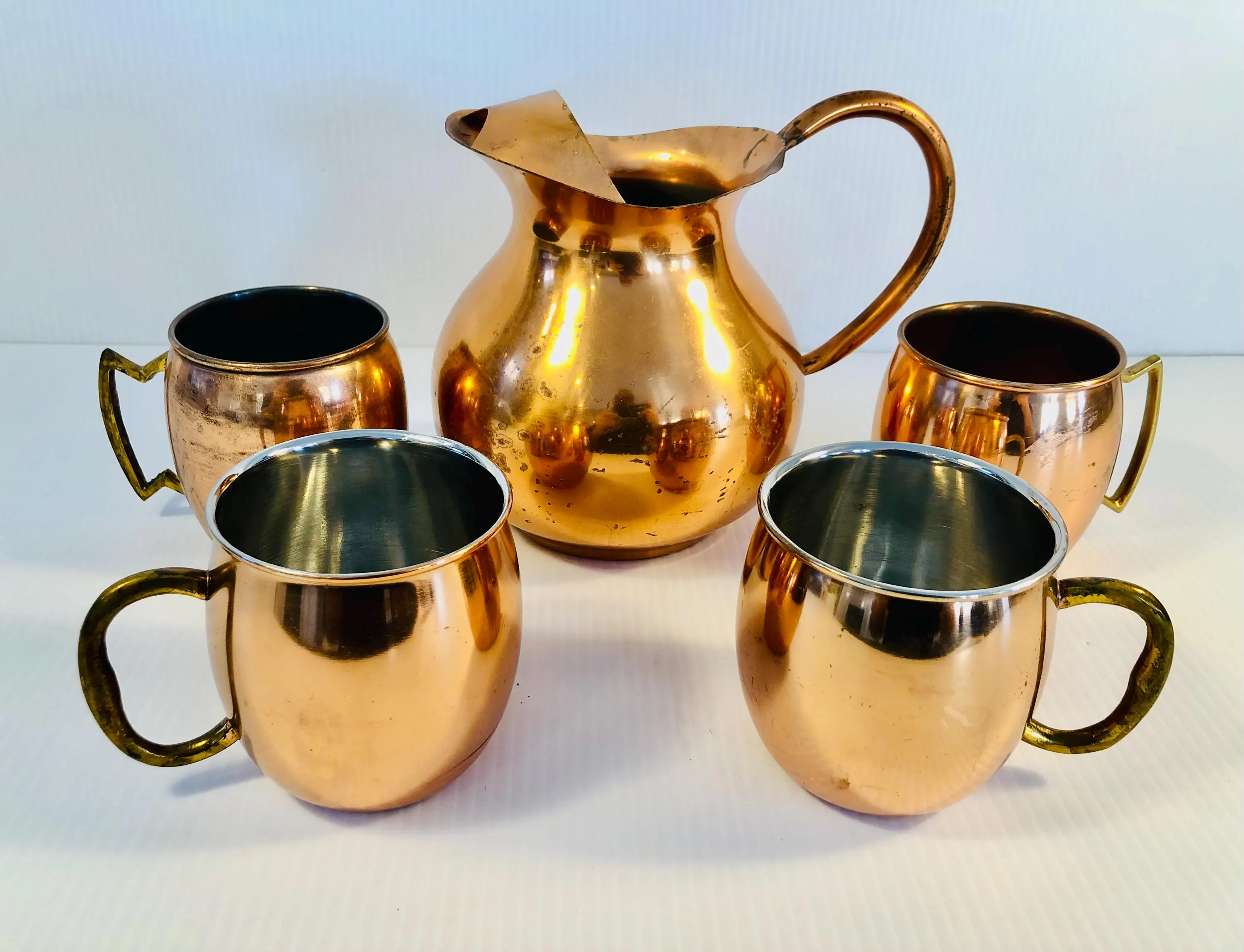 A condensation-covered glass pitcher of Moscow mules with lime wheels and mint on a bright kitchen counter, copper mugs and ice nearby, natural window light