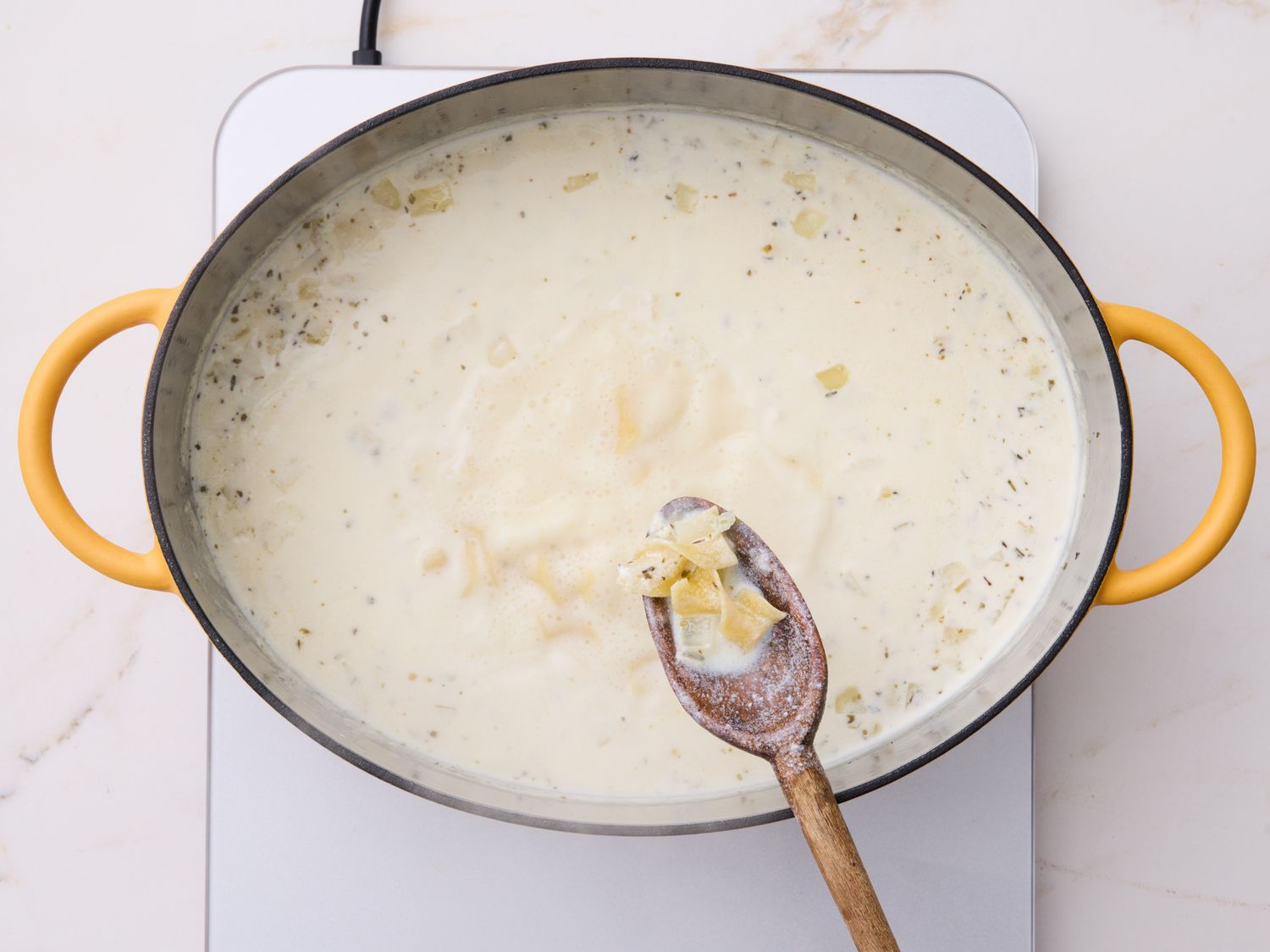 A cook stirring a pot of creamy sausage and potato soup on a stovetop with steam rising