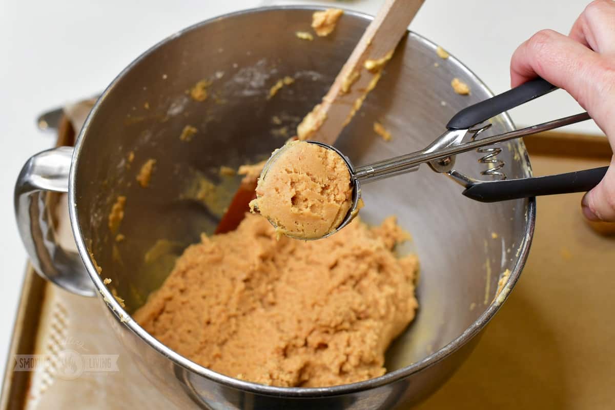 A cookie scoop portioning peanut butter cookie dough onto a parchment lined baking sheet on a kitchen counter