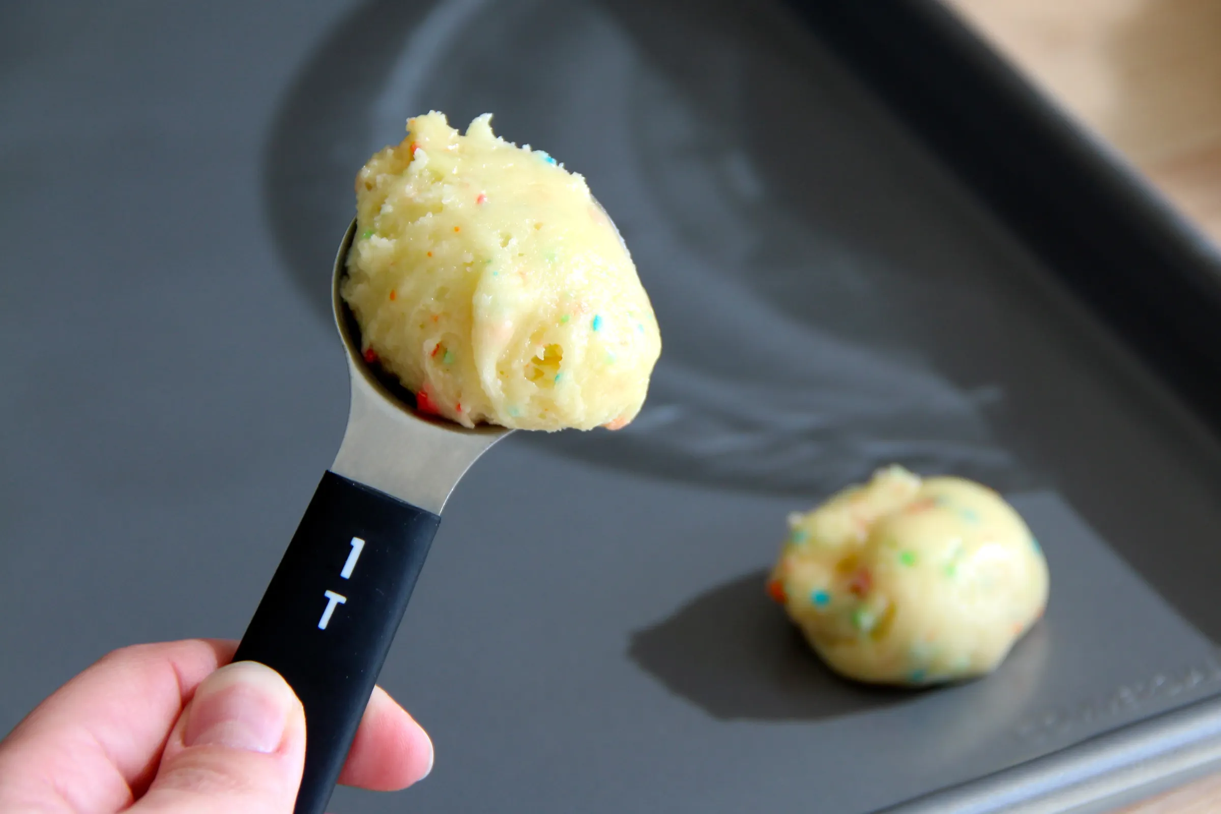 A cookie scoop portioning thick cake mix cookie dough onto a parchment-lined baking sheet