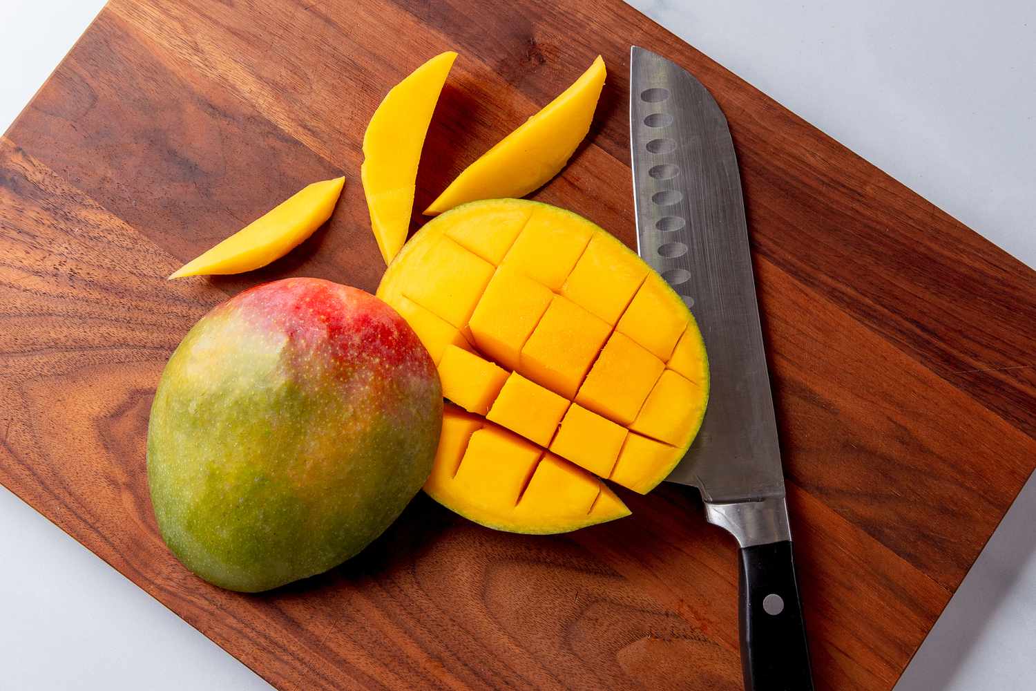 A cook's hands slicing a ripe mango on a wooden cutting board on a bright kitchen counter, with a bowl of sticky rice nearby in consistent natural light