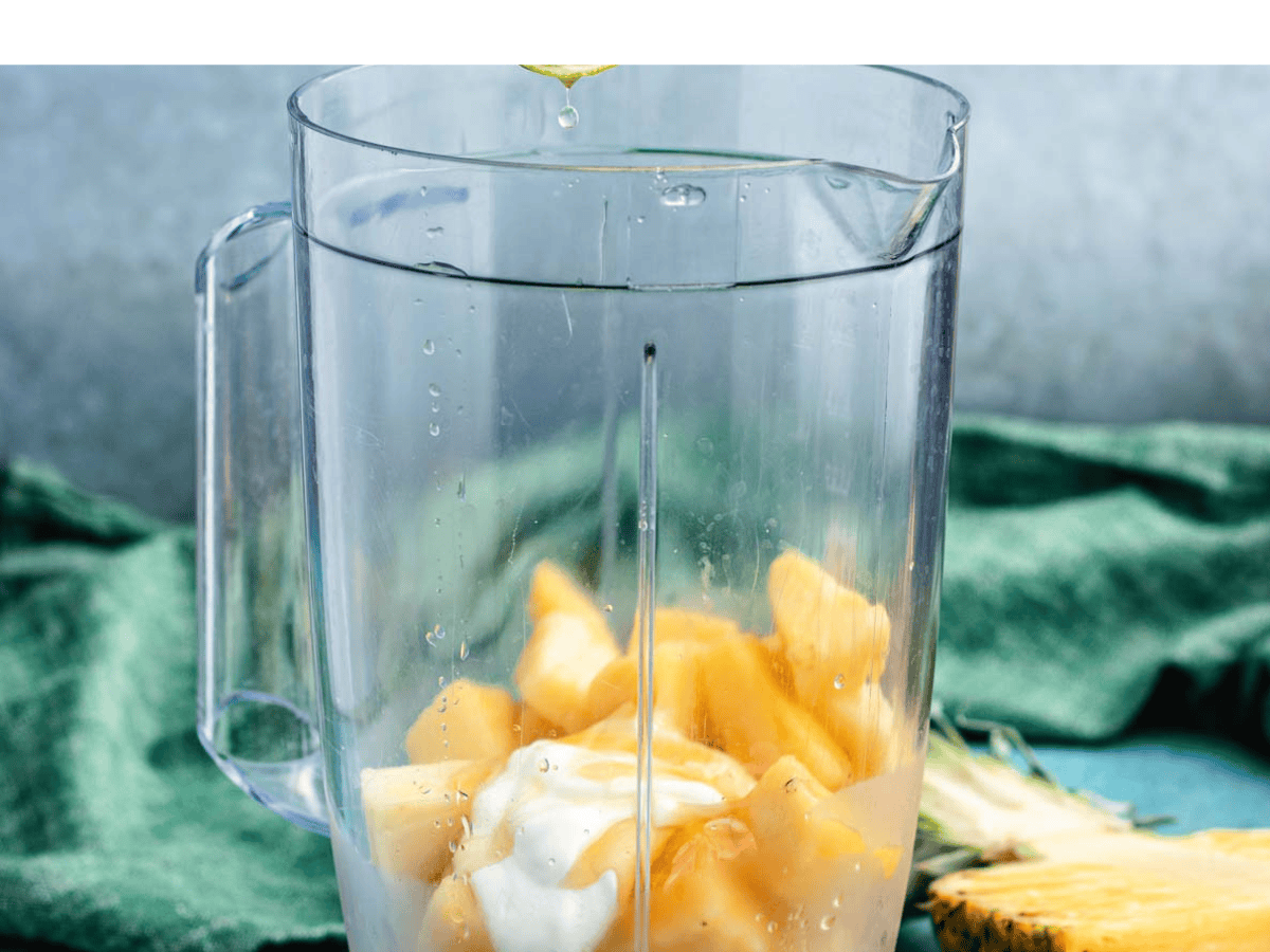 A countertop blender jar filled with milk, yogurt, banana, and frozen pineapple chunks before blending