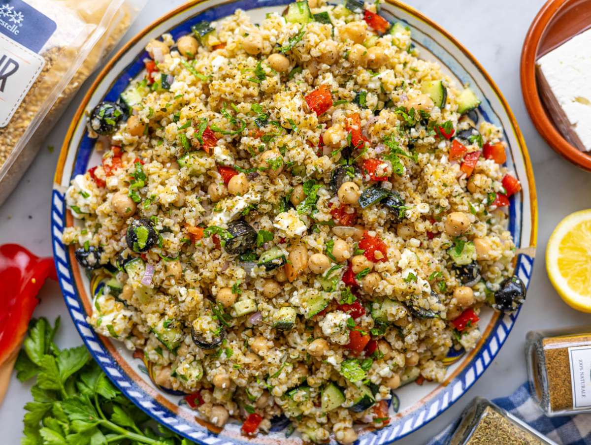 A countertop setup with chickpeas, fresh parsley, a whole lemon, a bowl of bulgur, and small bowls of spices arranged for cooking