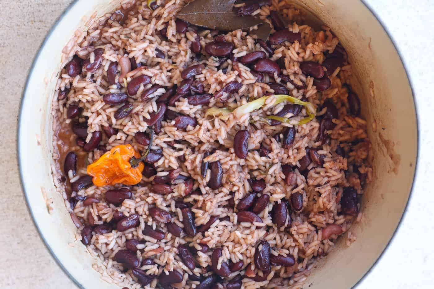 A covered pot on a stovetop gently simmering Jamaican rice and peas, with steam lightly fogging the lid in a cozy home kitchen