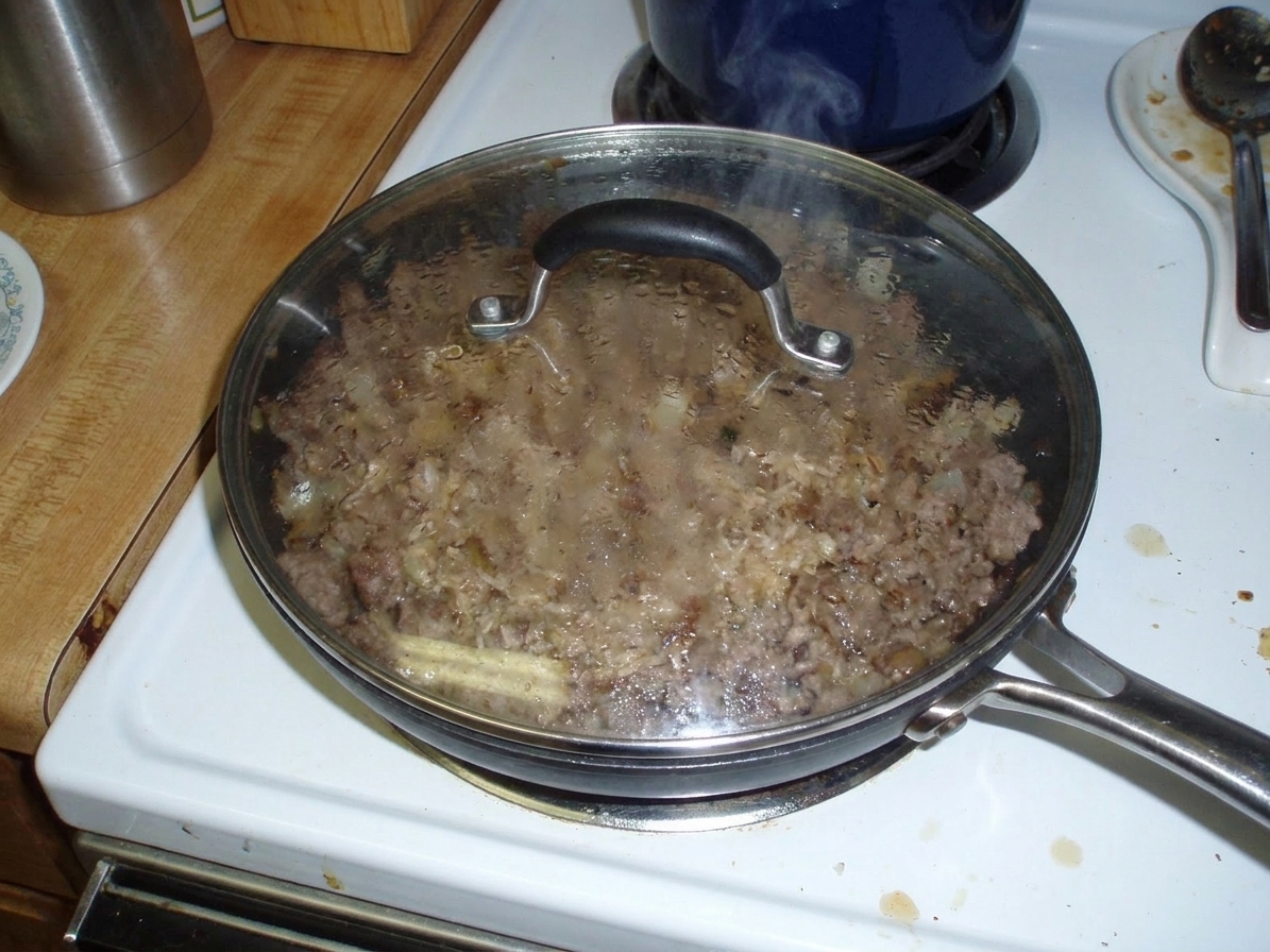 A covered skillet on a stovetop with steam rising slightly, indicating taco rice mixture simmering