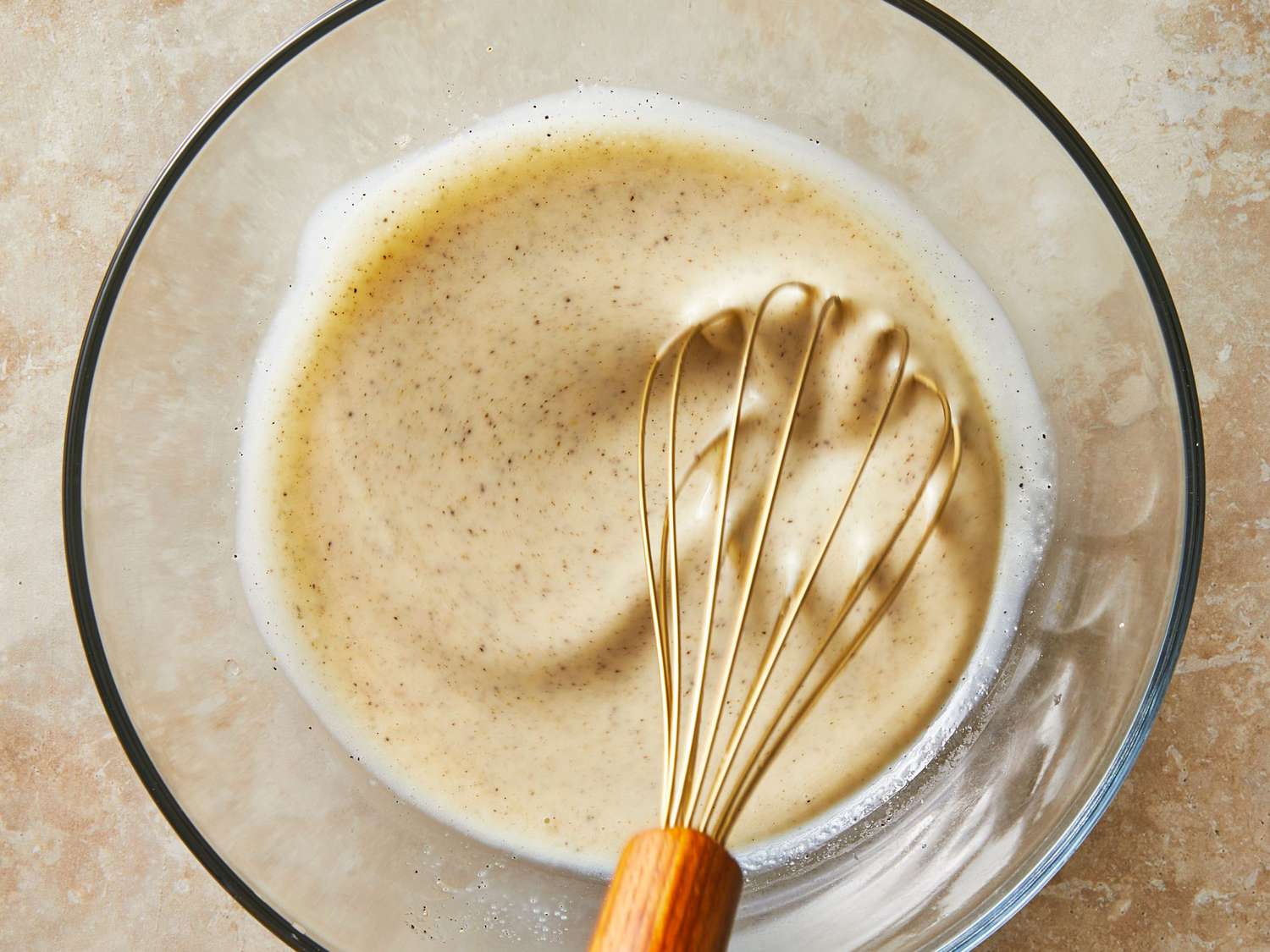 A creamy coleslaw dressing being whisked in a small bowl on a kitchen counter with ingredients nearby
