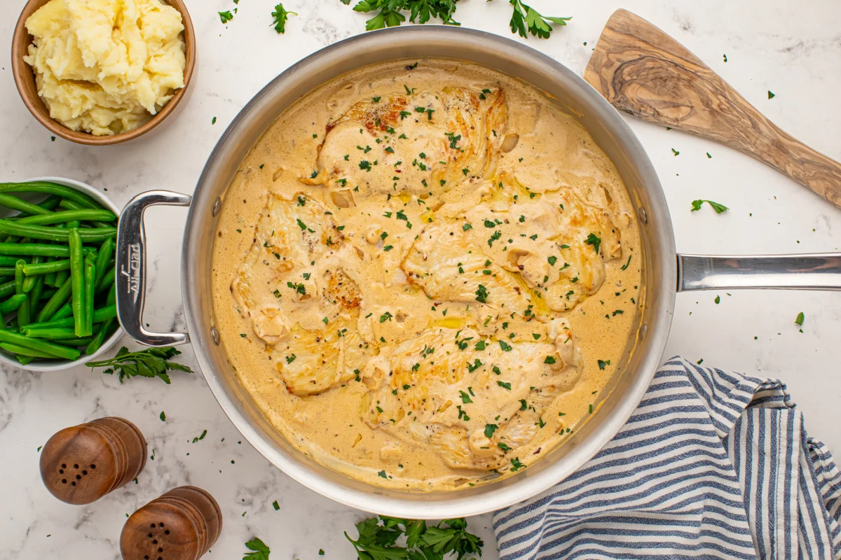 A creamy herb sauce being stirred in a skillet as Boursin cheese melts into hot pasta water, with a wooden spoon in motion