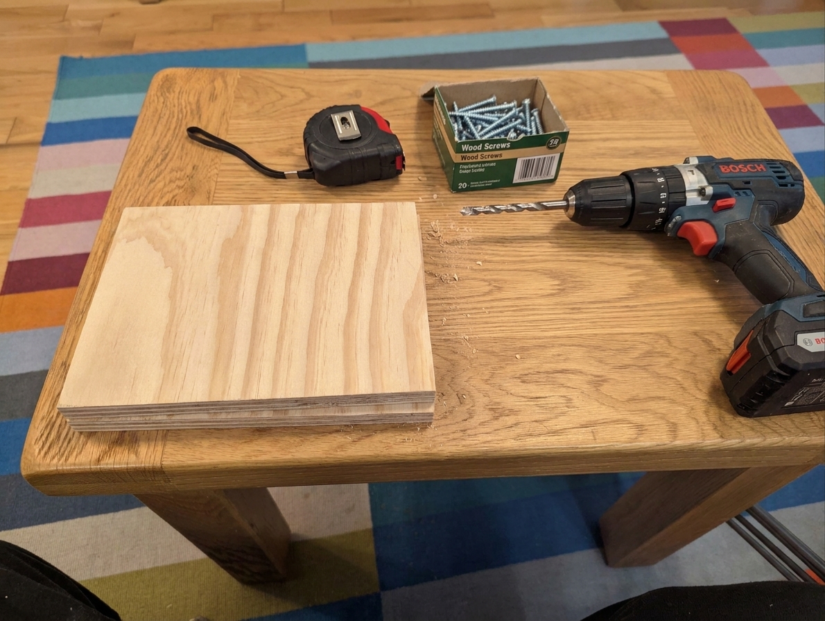 A cut 3/4 inch plywood panel on a kitchen table next to a tape measure, screws, and a cordless drill ready for a small bench build